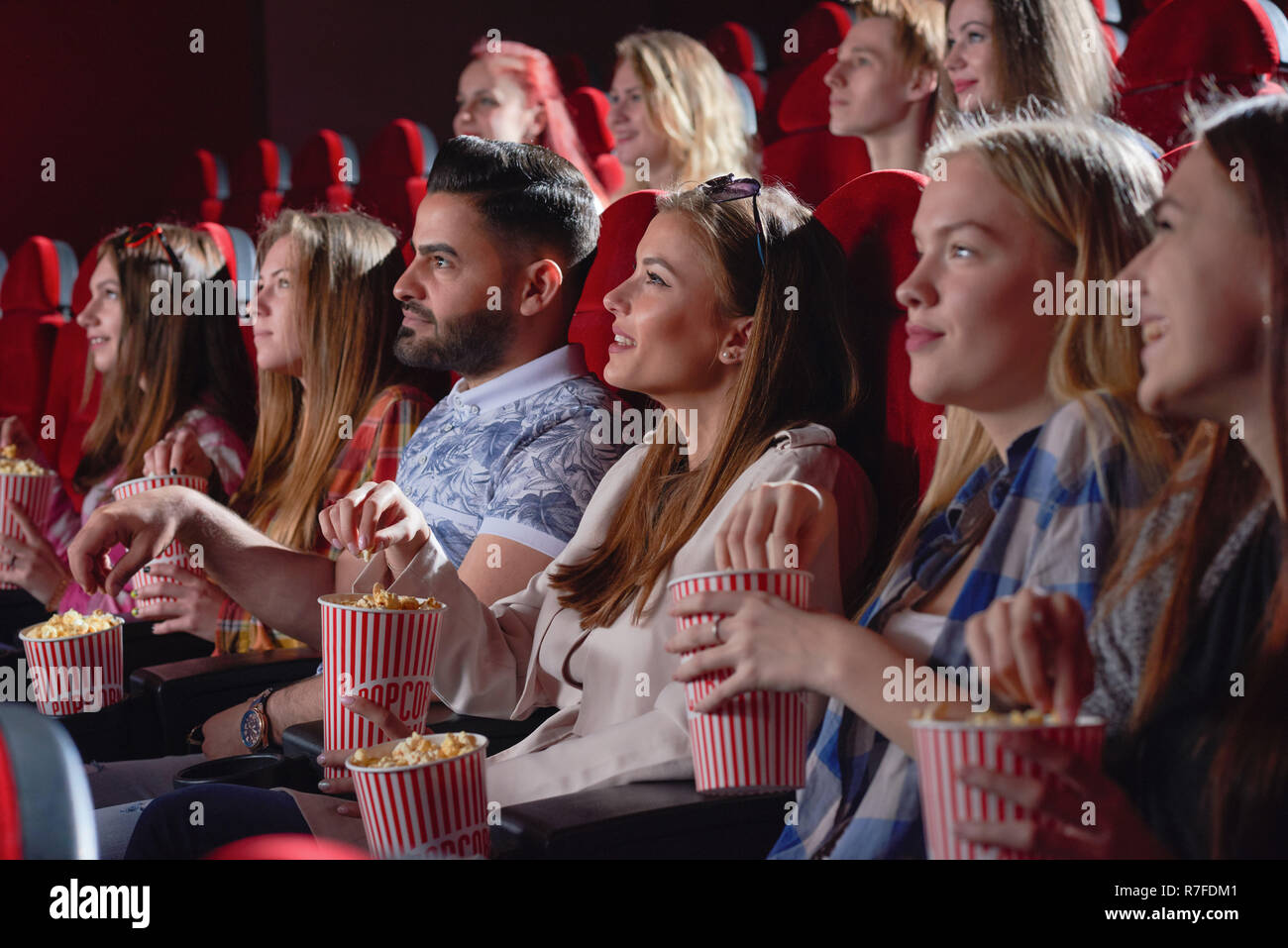 Groupe de jeunes et jolies femmes regardant nouvelle comédie divertissante dans la salle de cinéma. Cheerful young blonde rire, eating popcorn et bénéficiant d''tim Banque D'Images