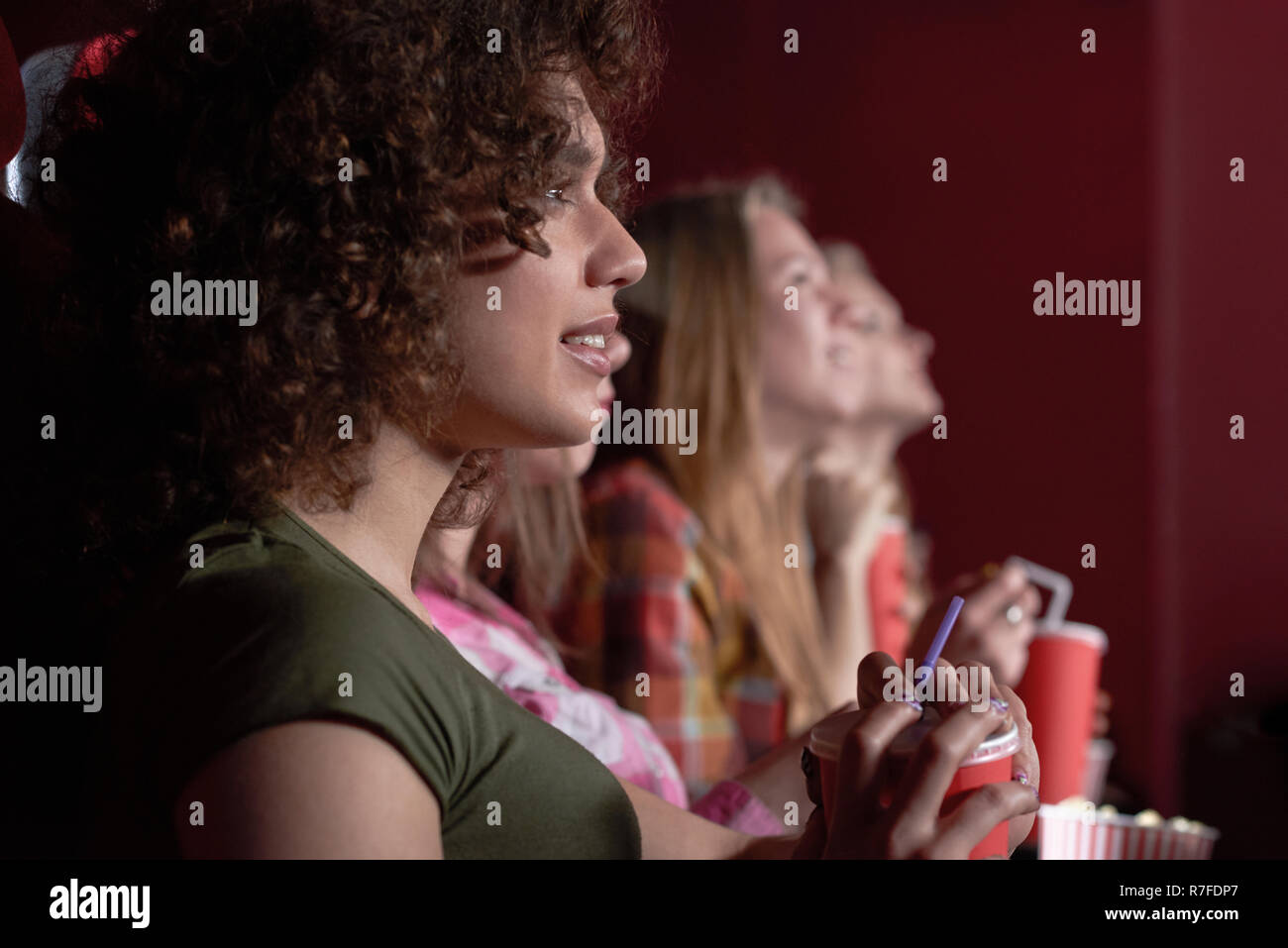 Vue latérale du beau dark haired girl enjoying regarder film intéressant au cinéma. Jolie femme viewer en chemise blanche et jeans à la recherche à l'écran, en gardant le pop-corn et souriant. Banque D'Images