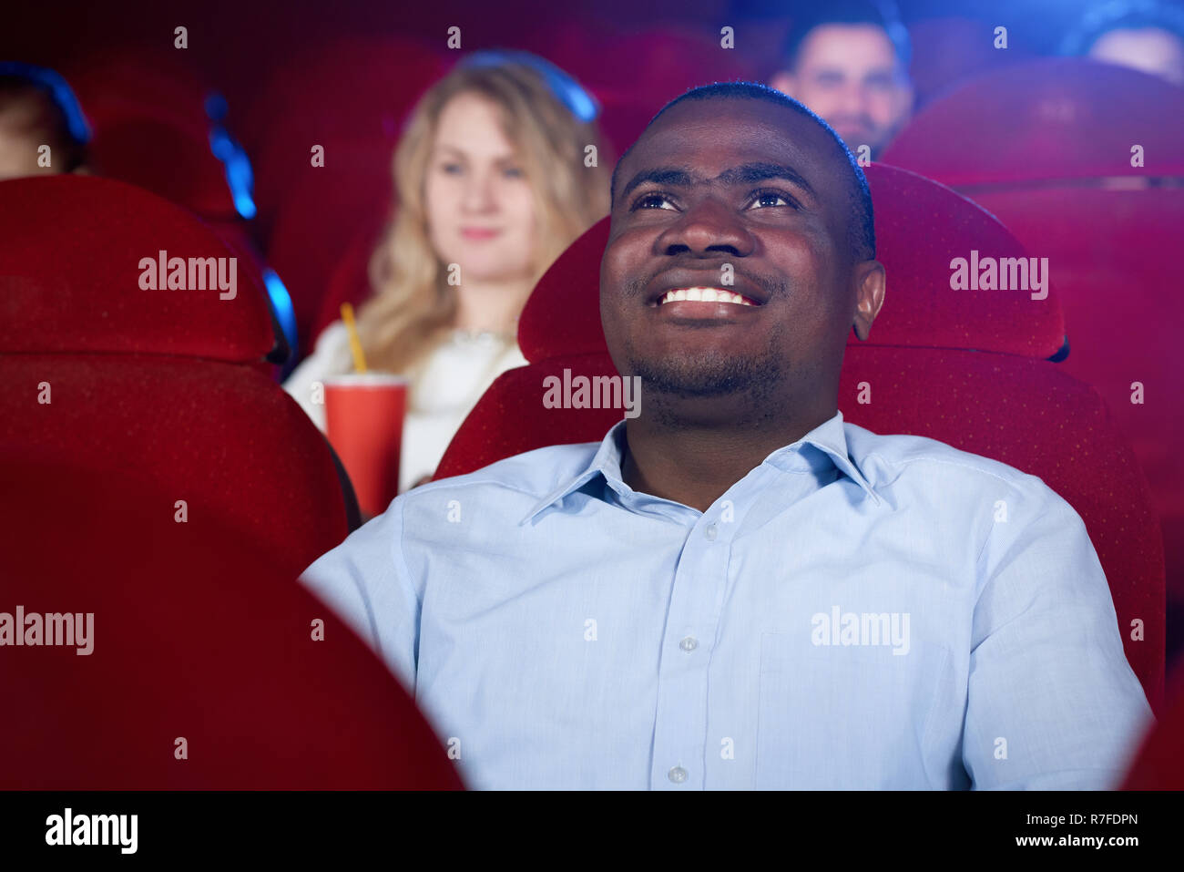 Vue de face de l'homme spectateur regardant intéressant film dans le cinéma. Jeune homme afro wearing blue shirt attendant final du film. Notion de divertissement et de loisirs. Banque D'Images