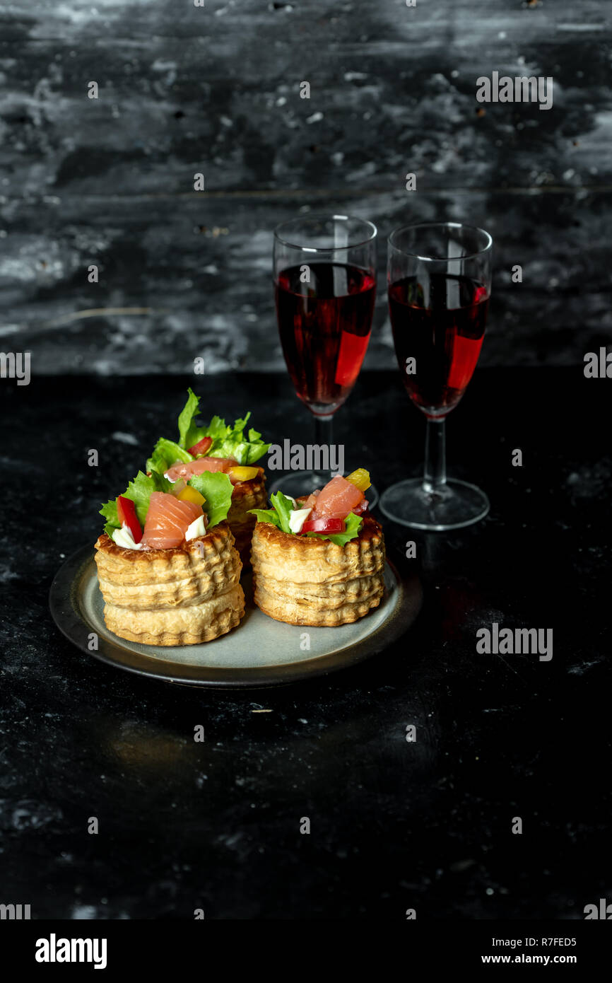 La cuisine française, les Galettes croquantes de laitue et de saumon fumé sur un fond sombre, rustique, à côté d'un verre de vin rouge Banque D'Images