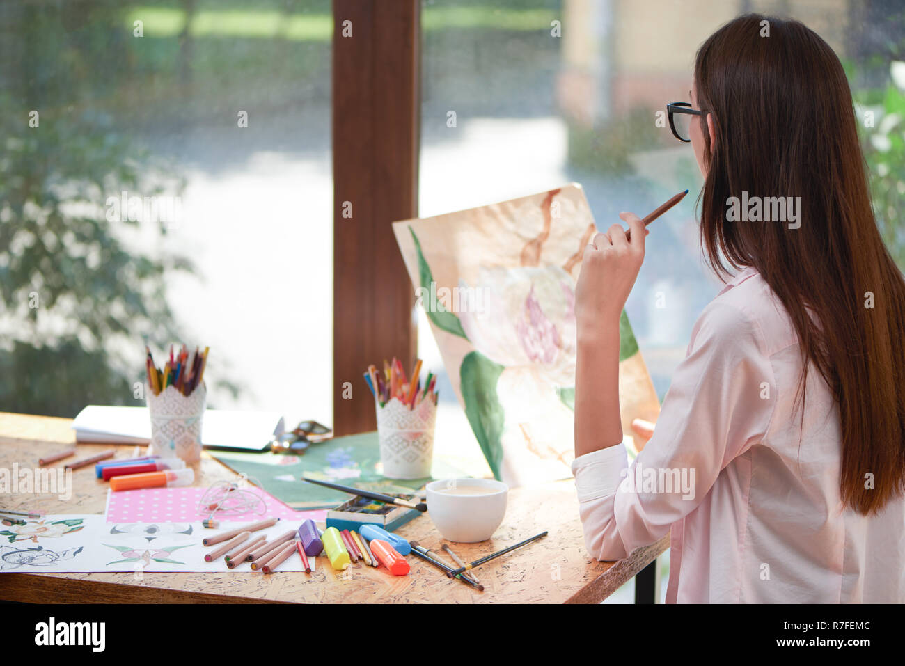 Jeune artiste à photo de fleur et la pensée. Méconnaissable woman holding crayon en main. Fille assise à table avec les fournitures du peintre comme marqueurs, brosses et feuilles de papier. Banque D'Images