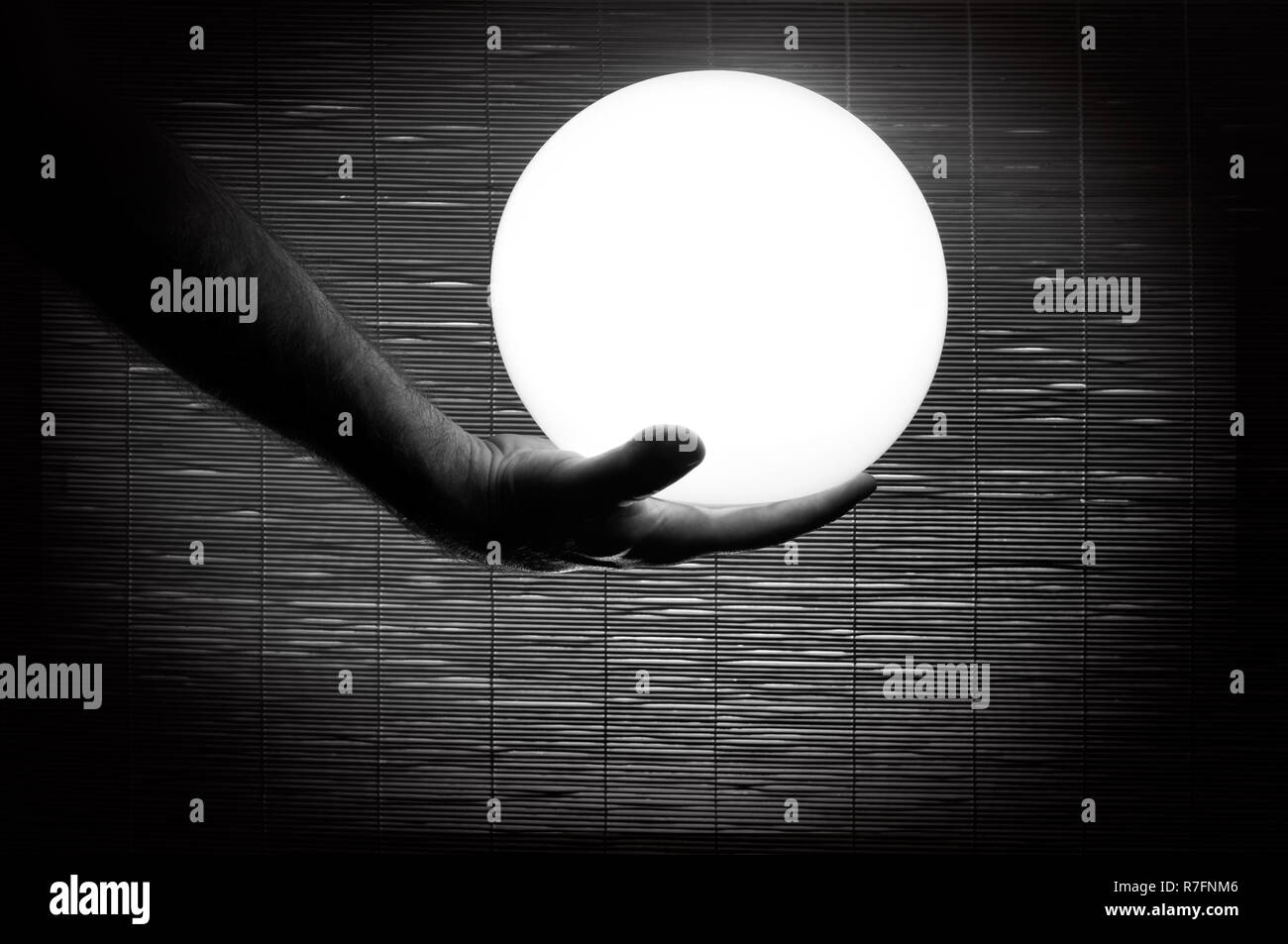 La main de l'homme tenant une sphère blanche fond bambou tourné en noir et blanc Banque D'Images