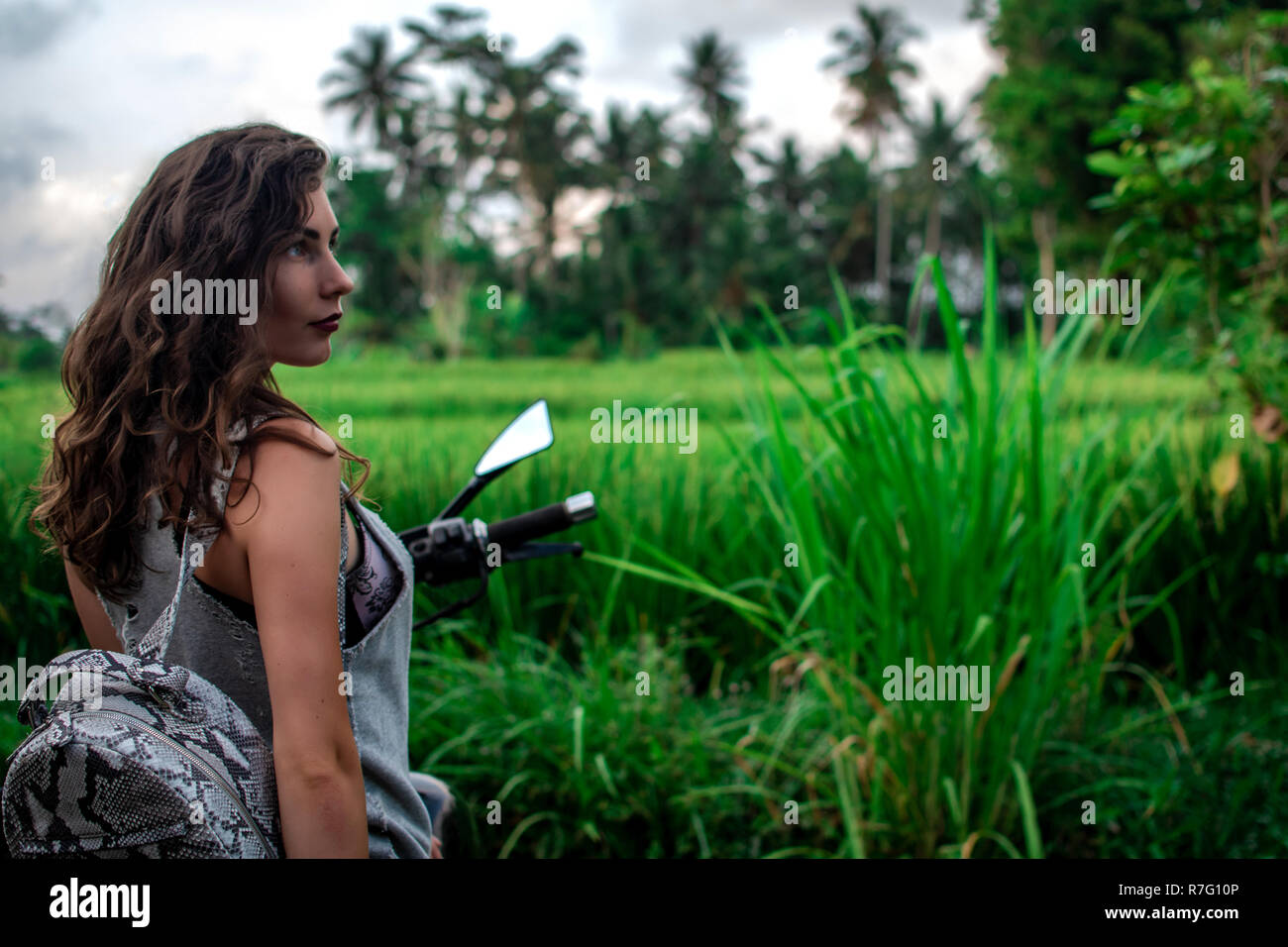 Une femme assise sur un vélo près d'un paysage fantastique, jungle, forêt tropicale en face d'elle et la nature.Concept de style, la mode dans l'aventure et les voyages avec accessoire python Banque D'Images