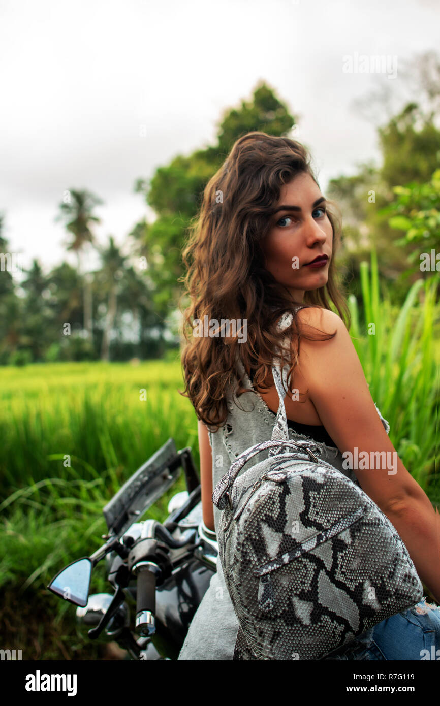 Une femme assise sur un vélo près d'un paysage fantastique, jungle, forêt tropicale en face d'elle et la nature.Concept de style, la mode dans l'aventure et les voyages avec accessoire python Banque D'Images