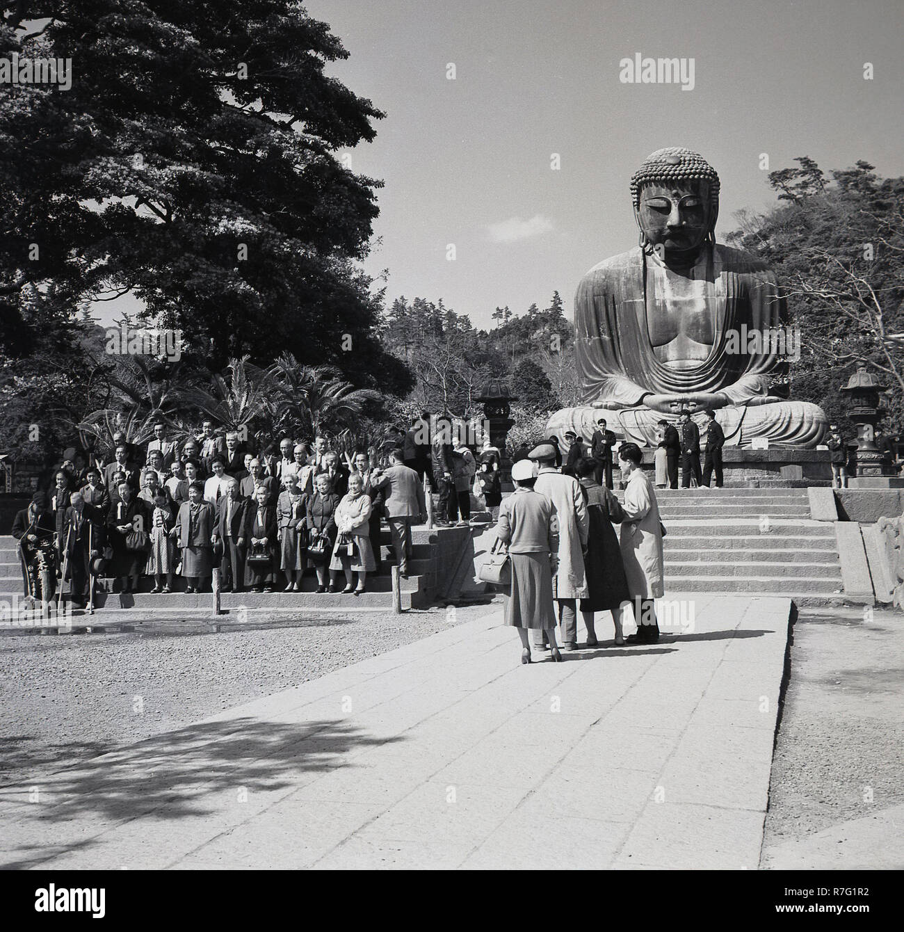 Années 1950, histrical, les touristes japonais se posent pour une photo de groupe devant le grand Bouddha de Kamakura. Cette gigantesque statue en bronze d'Amida Buddha se trouve dans l'enceinte de l'Kotokuin temple, Kanagawa, Japon. Banque D'Images
