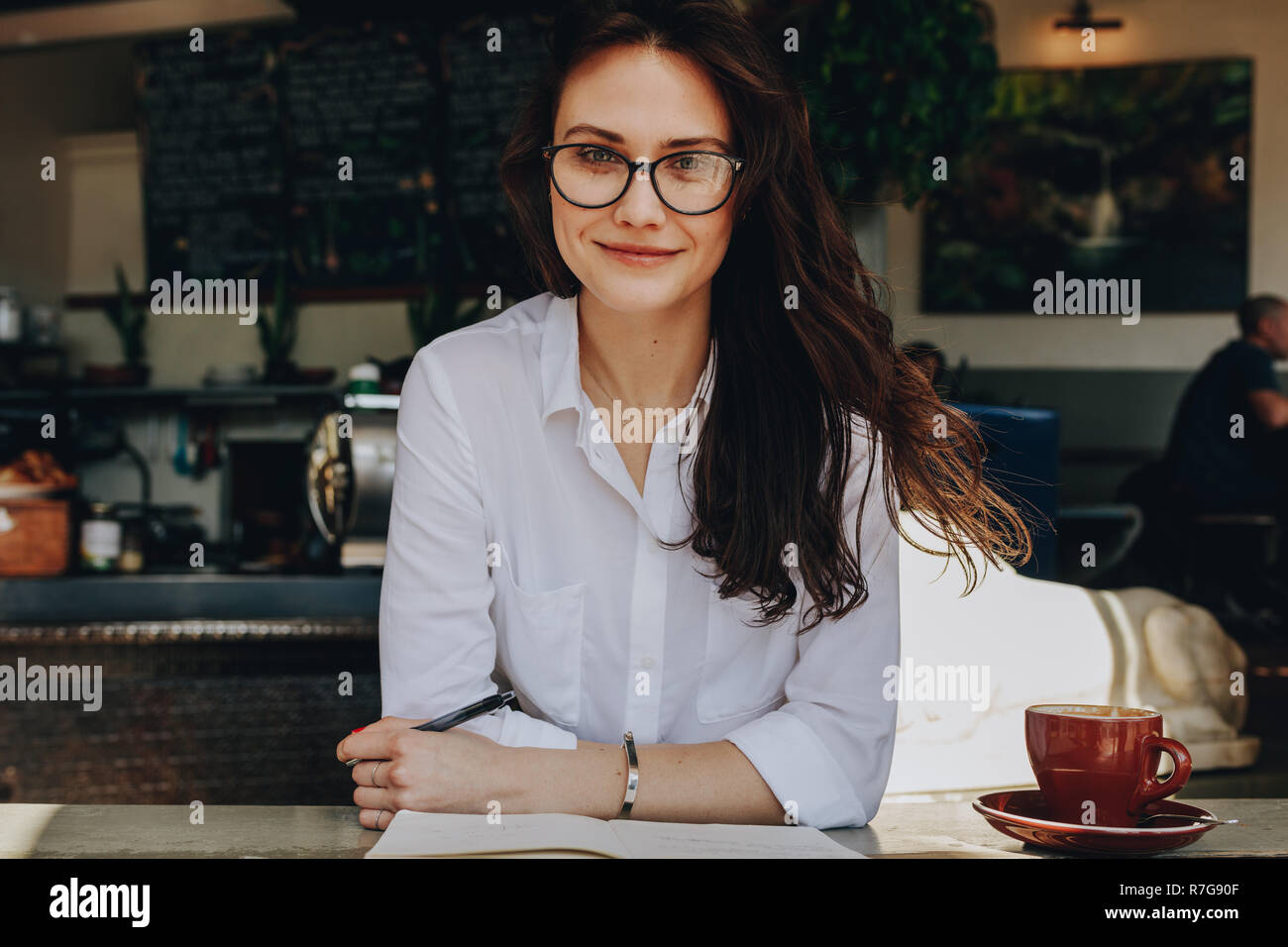 Portrait de femme attrayante assis à café avec ordinateur portable et tasse de café sur la table. Les femmes de race blanche en chemise blanche et les lunettes en relaxant fac Banque D'Images