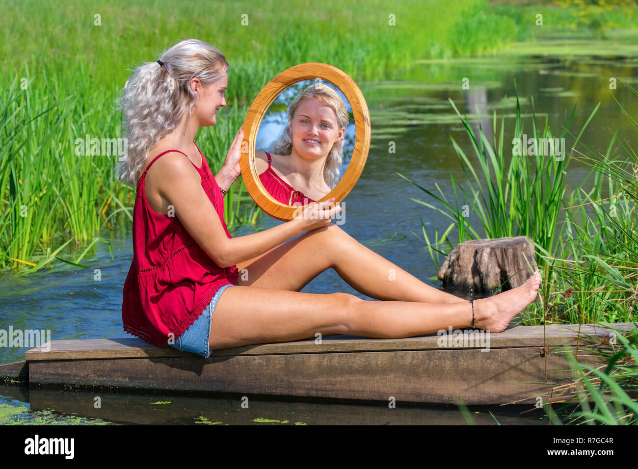 Young blonde woman sitting avec miroir à l'eau dans la nature libre Banque D'Images