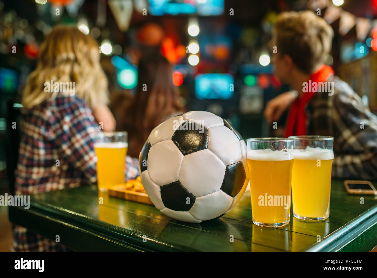 Ball et de la bière sur la table dans un bar sportif, les fans de football sur l'arrière-plan. La diffusion TV, regarder le jeu concept Banque D'Images