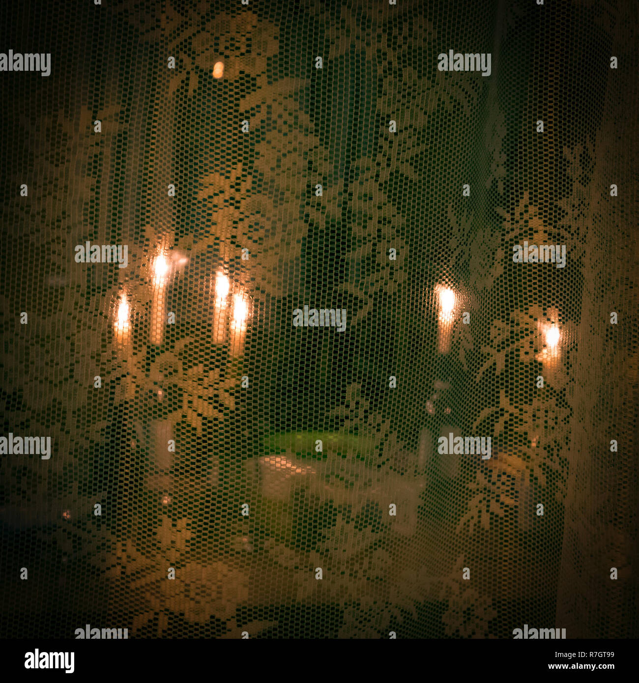 Un certain nombre de bougies allumées dans des bouteilles derrière le rideau de dentelle transparent, fond de Noël romantique dans des tons verts Banque D'Images