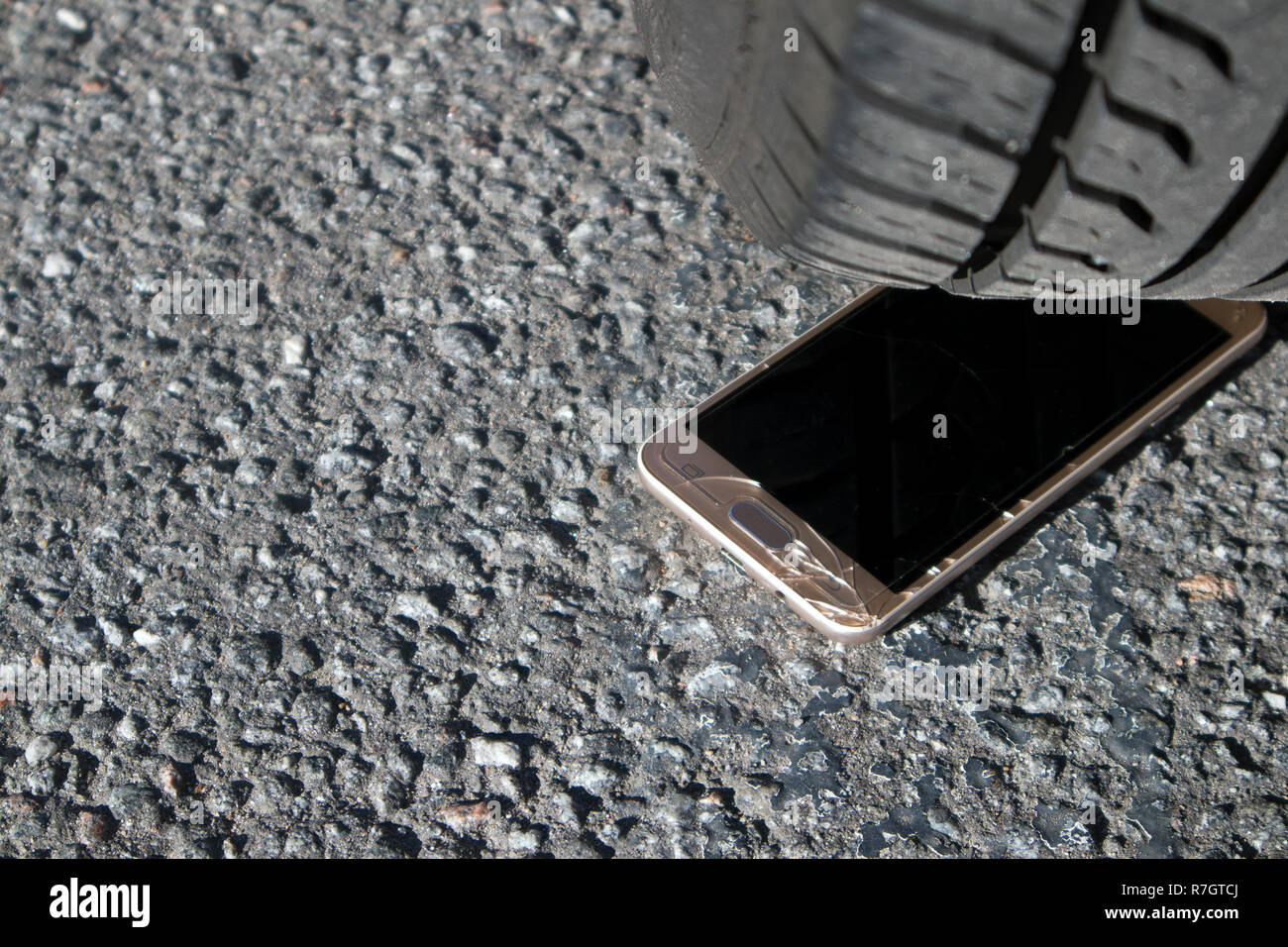 Smart phone moderne en verre avec écran brisé sur l'asphalte sous les roues de voiture Banque D'Images