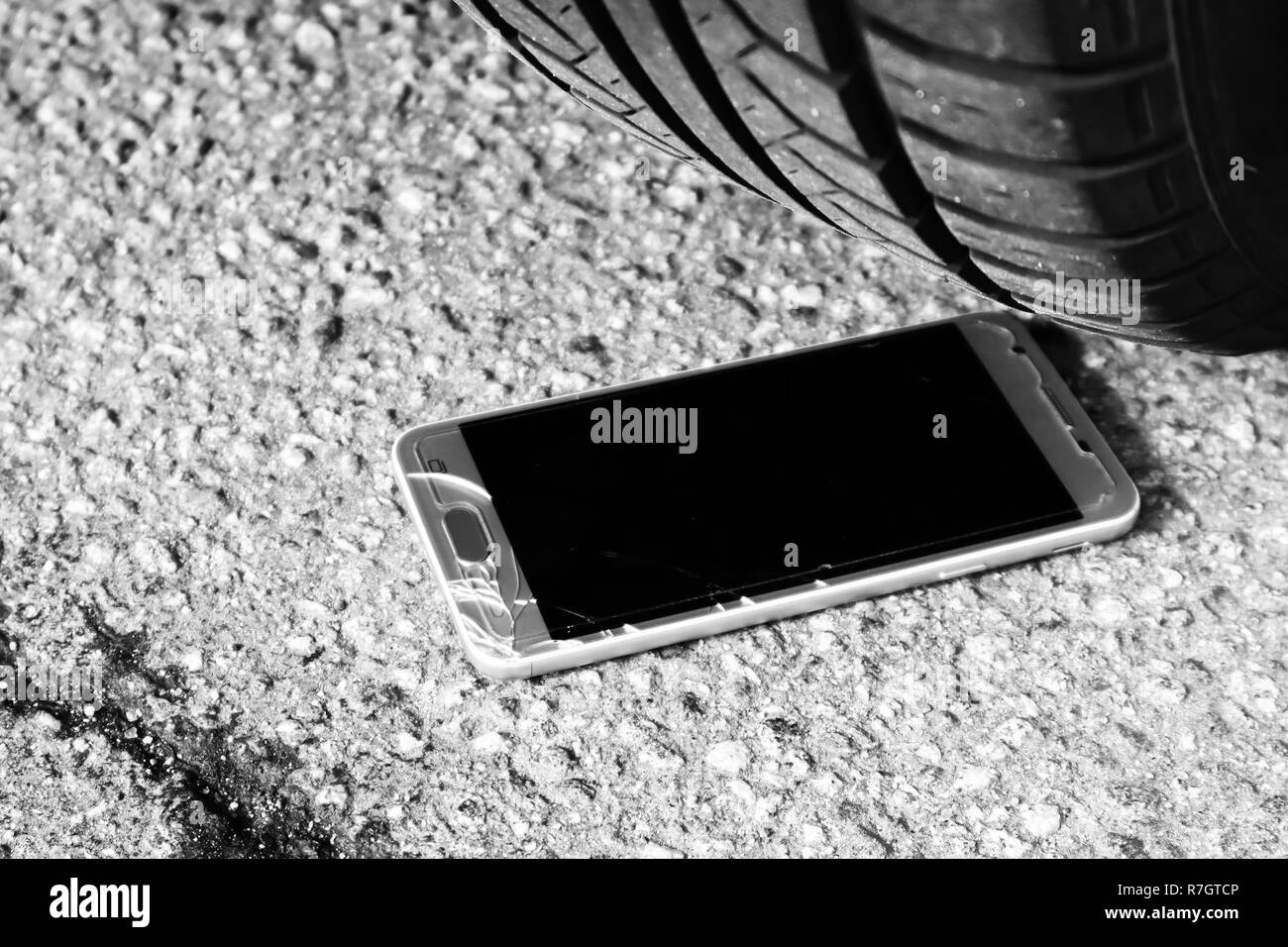 Smart phone moderne en verre avec écran brisé sur l'asphalte sous les roues de voiture Banque D'Images