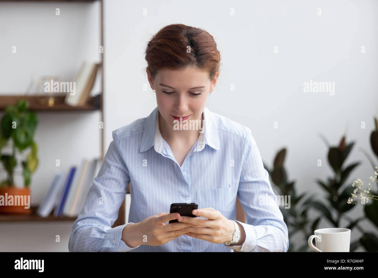 Femme assise dans la salle de bureau message lecture holding smartphone Banque D'Images