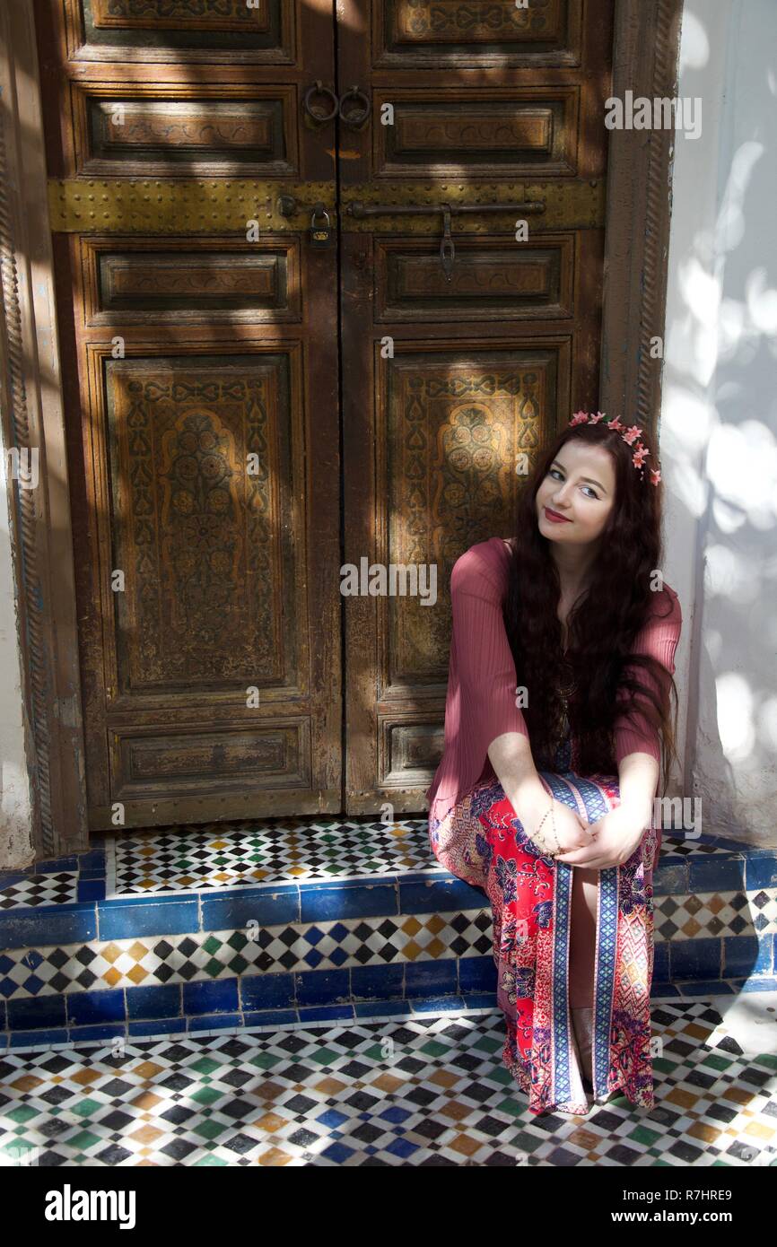 Un long haired brunette girl hippie rose, rouge et de fleurs se trouve dans un sol carrelé porte au Maroc Banque D'Images