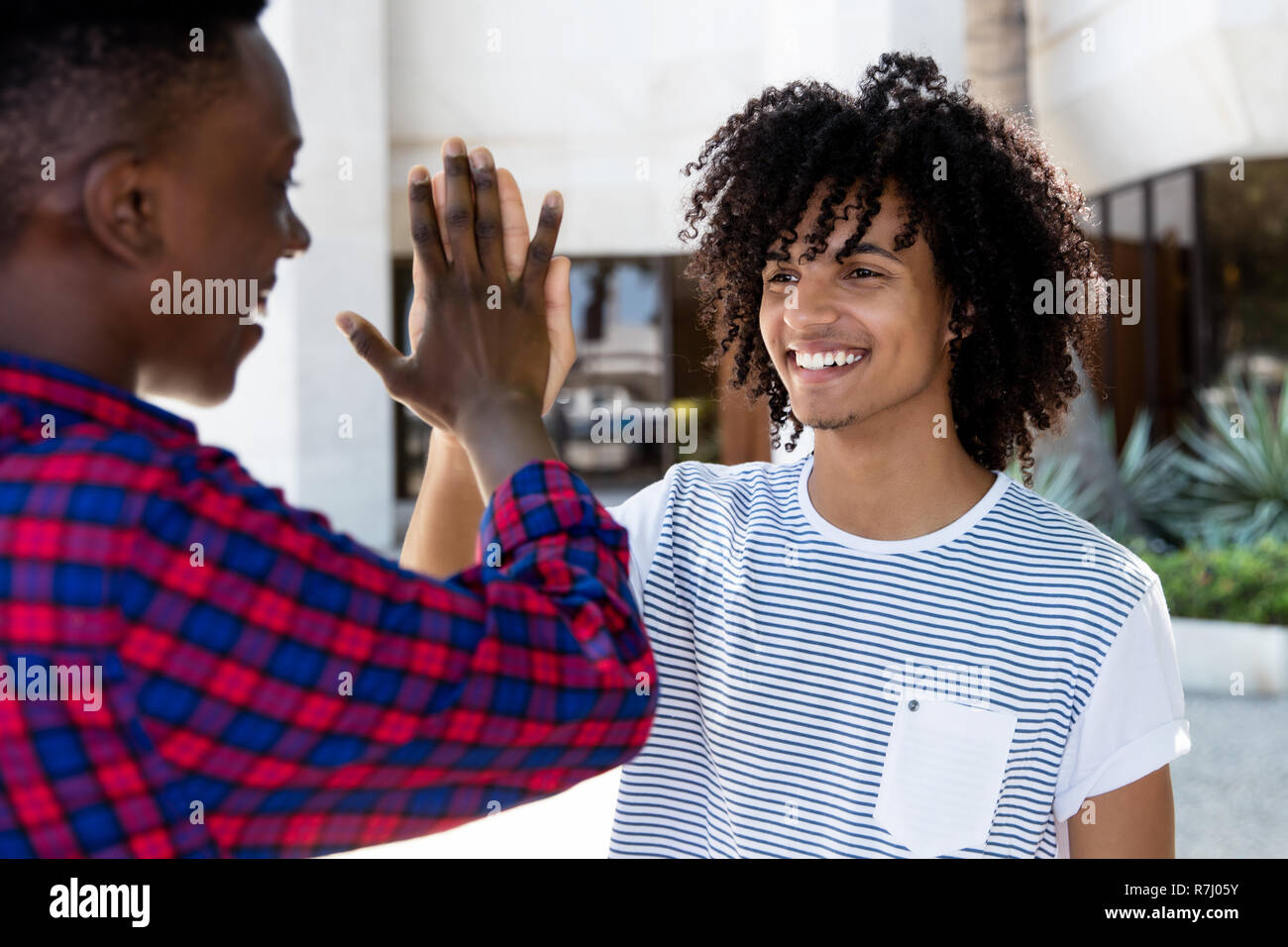 Young adult man with long hair high five pour donner à l'extérieur de l'Afrique de l'ami dans la ville Banque D'Images