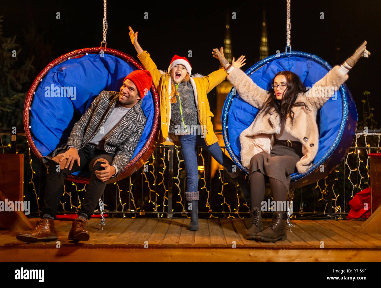 Couple et sa fille s'amusant sur la pendaison chaises Noël, Zagreb, Croatie. Banque D'Images