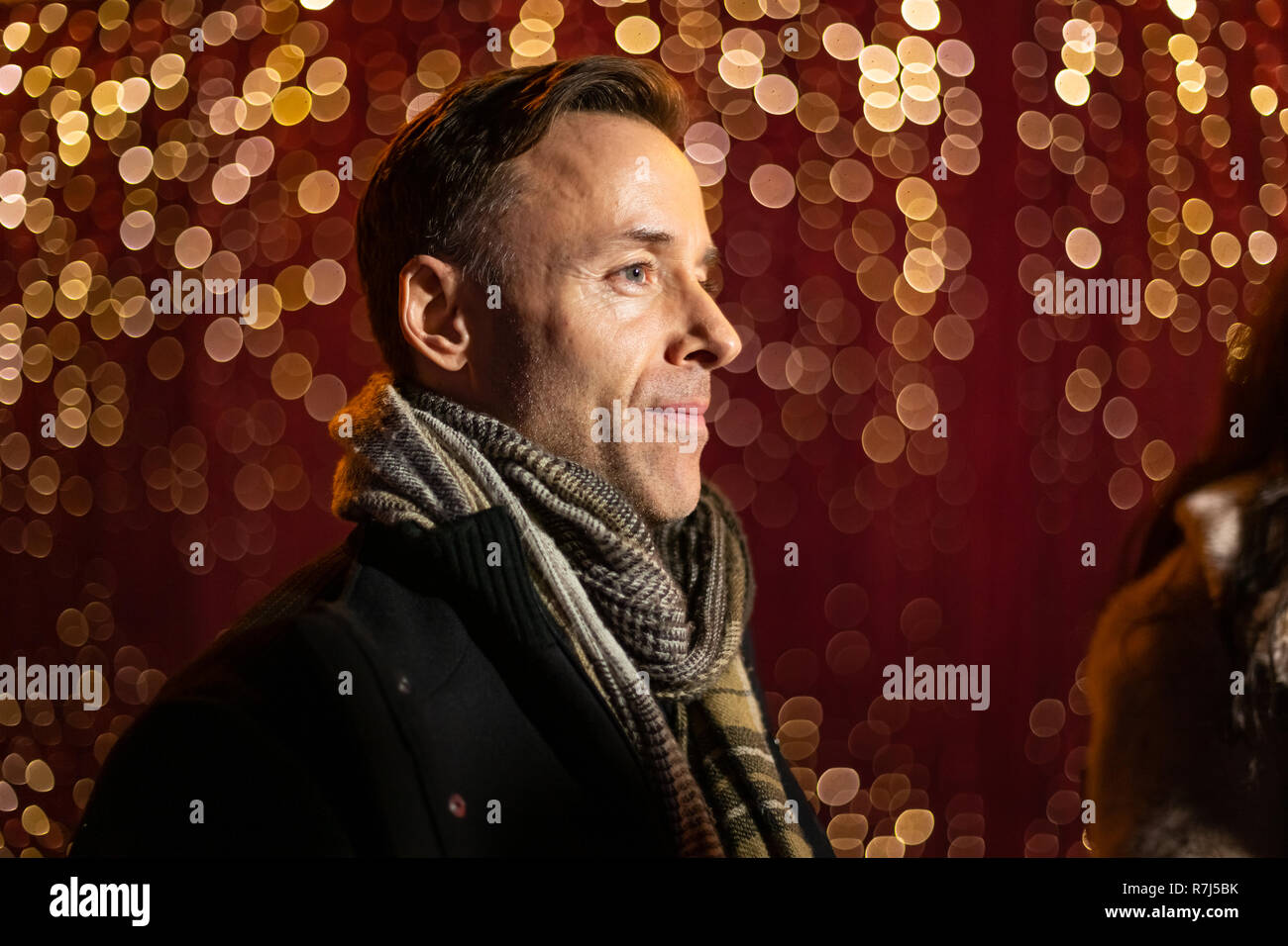 Homme posant pour la photo devant la lumière de mur à Marché de Noël. Banque D'Images