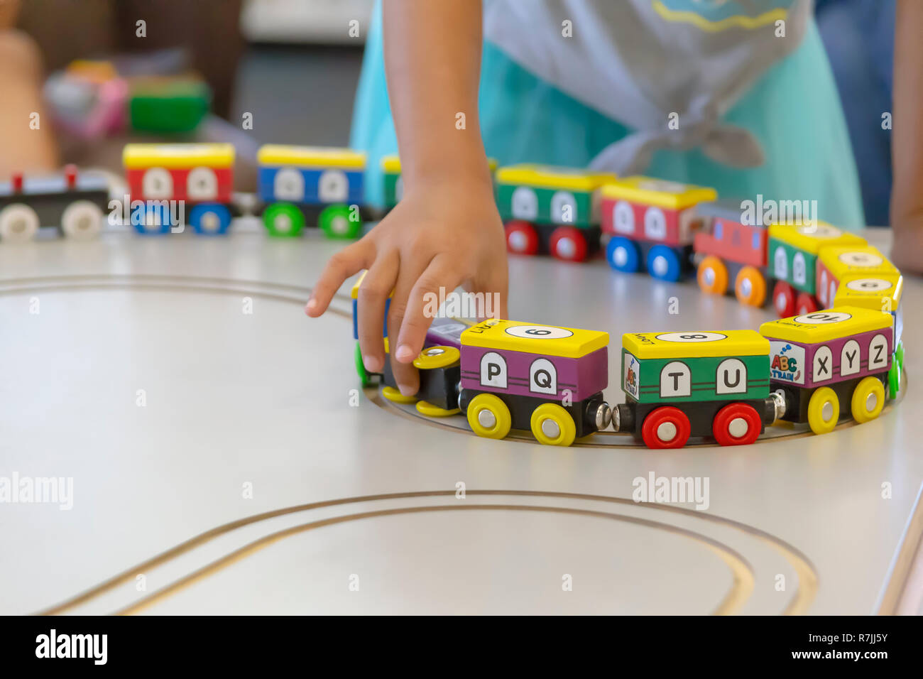 Libre d'un jeune enfant en tirant un train en bois sculpté au-dessus d'une table. Le train a coloré les lettres de l'alphabet peint. Banque D'Images