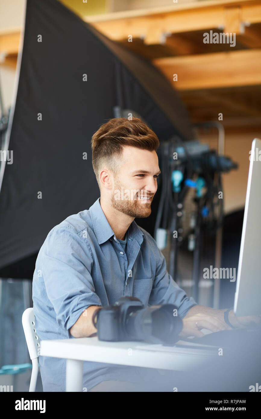 Vue de côté portrait de beau mâle photographe travaillant en studio à l'aide d'ordinateur contre le matériel d'éclairage Banque D'Images