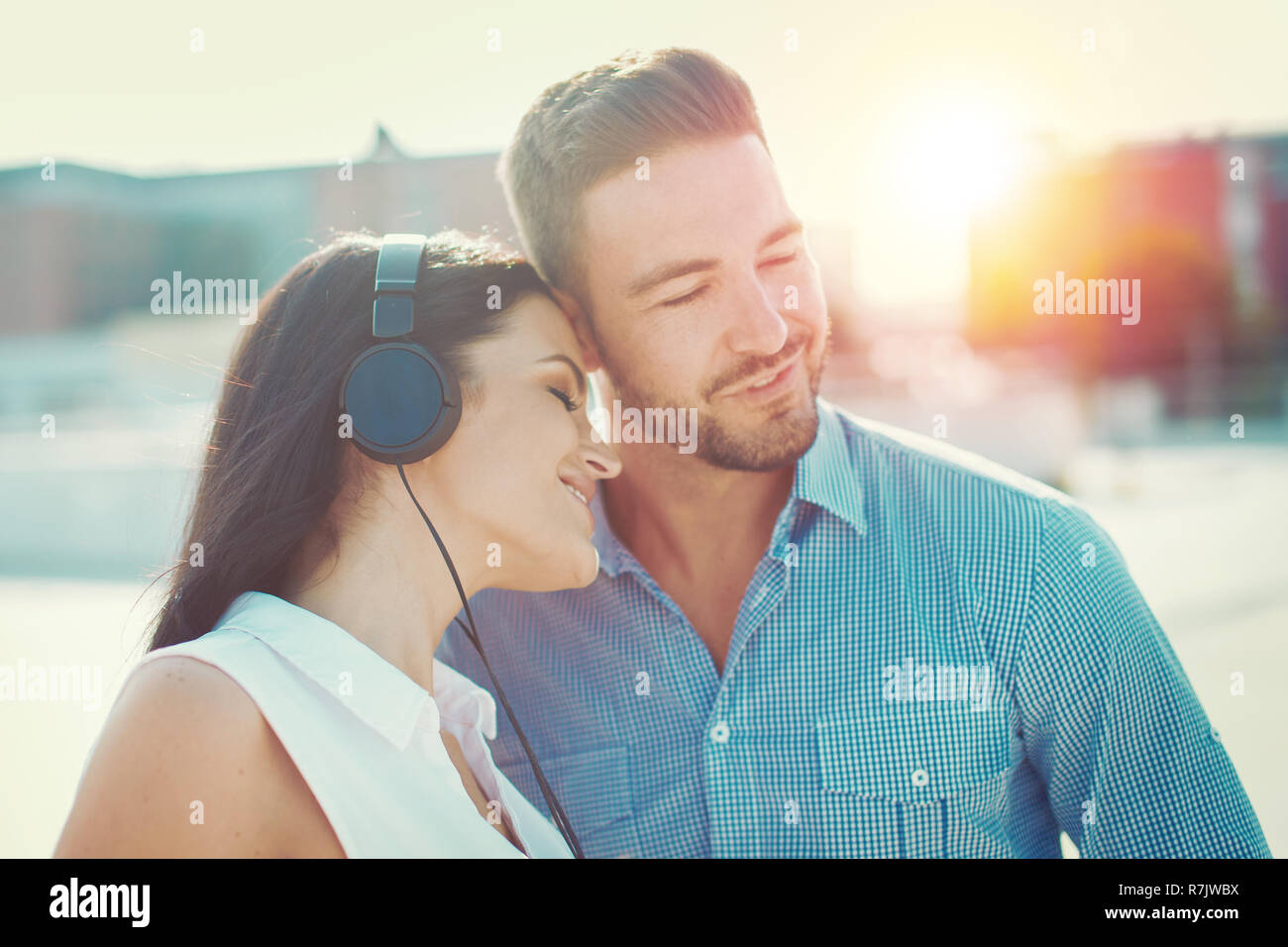 Jeune couple sympathique à l'écoute de la musique avec des écouteurs à l'extérieur, chantant une chanson Banque D'Images