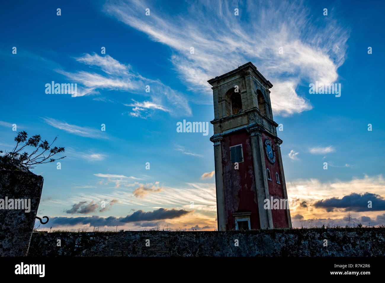 Tour de l'horloge médiévale dans le fort de Corfou, Grèce au coucher du soleil avec le soleil bas à l'arrière de l'immeuble, paysage nuageux ciel printemps coloré Banque D'Images