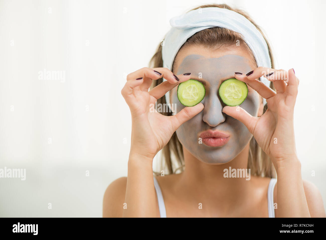 Belle jeune femme dans l'argile masque de boue sur le visage couvrant les yeux avec des tranches de concombre. Banque D'Images
