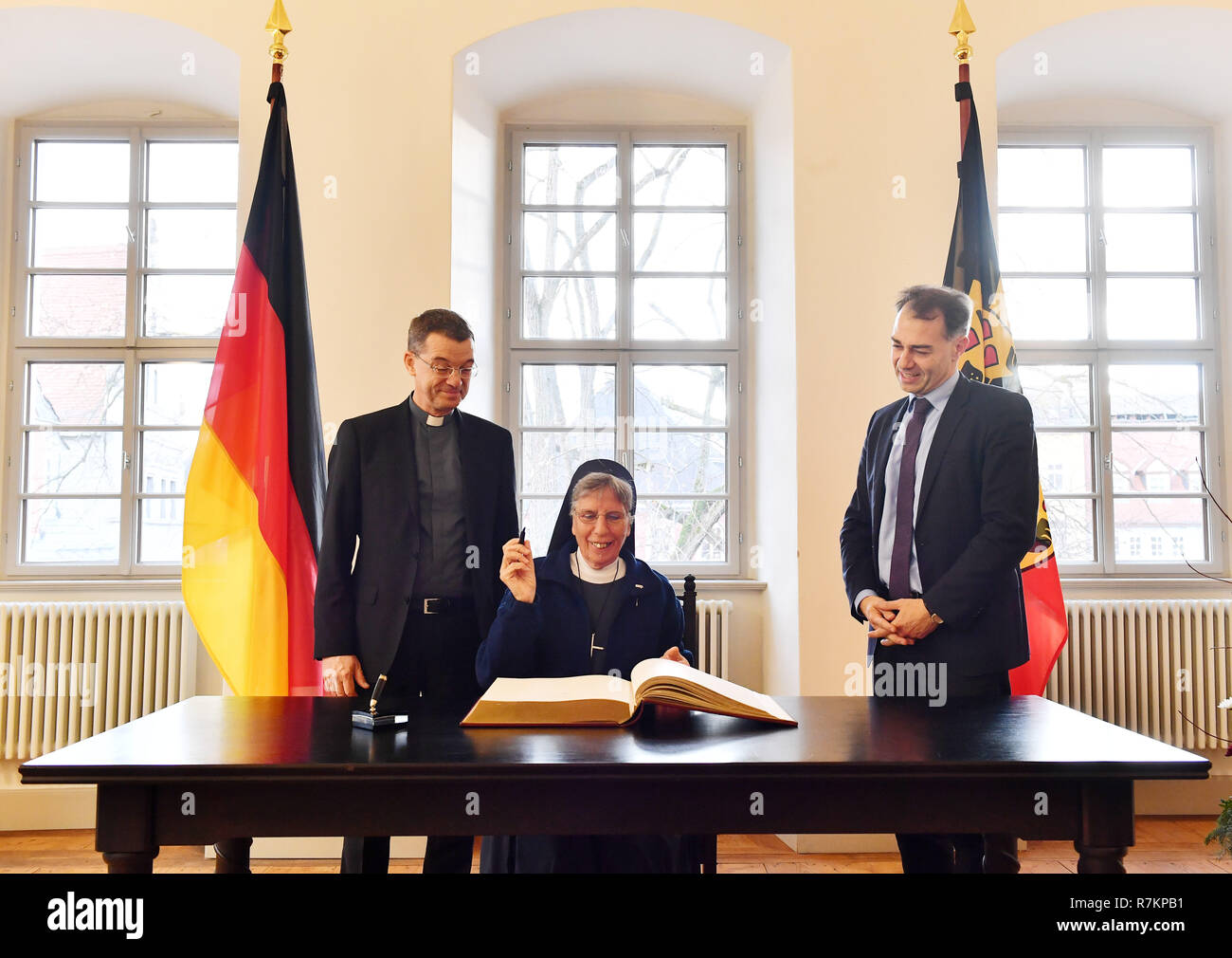 10 décembre 2018, la Thuringe, Weimar : Sœur Lorena Jenal (M) signe le livre d'or de la ville de Weimar avant de recevoir le Prix des droits de l'homme de Weimar, Klaus Krämer (l), Président de la Société missionnaire catholique internationale missio e.V., et le seigneur de Weimar le Maire Peter Kleine (r., non partisane) se tenir à côté d'elle. La ville de Weimar awards le prix à la nonne Suisse le même jour. La ville est donc rendre hommage à leur engagement pour les victimes de la chasse aux sorcières en Papouasie Nouvelle Guinée. L'organisation de secours catholique Missio avait désigné le Swiss pour le prix. Photo : Martin Schutt/dpa-Zentr Banque D'Images