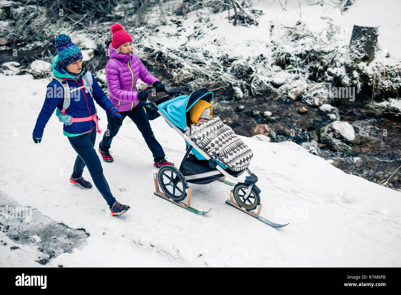 Deux femmes avec poussette de bébé profiter de la maternité dans la forêt d'hiver, paysage montagneux. Mère de la randonnée avec un partenaire et un enfant en blanc Snowy Woods. Banque D'Images