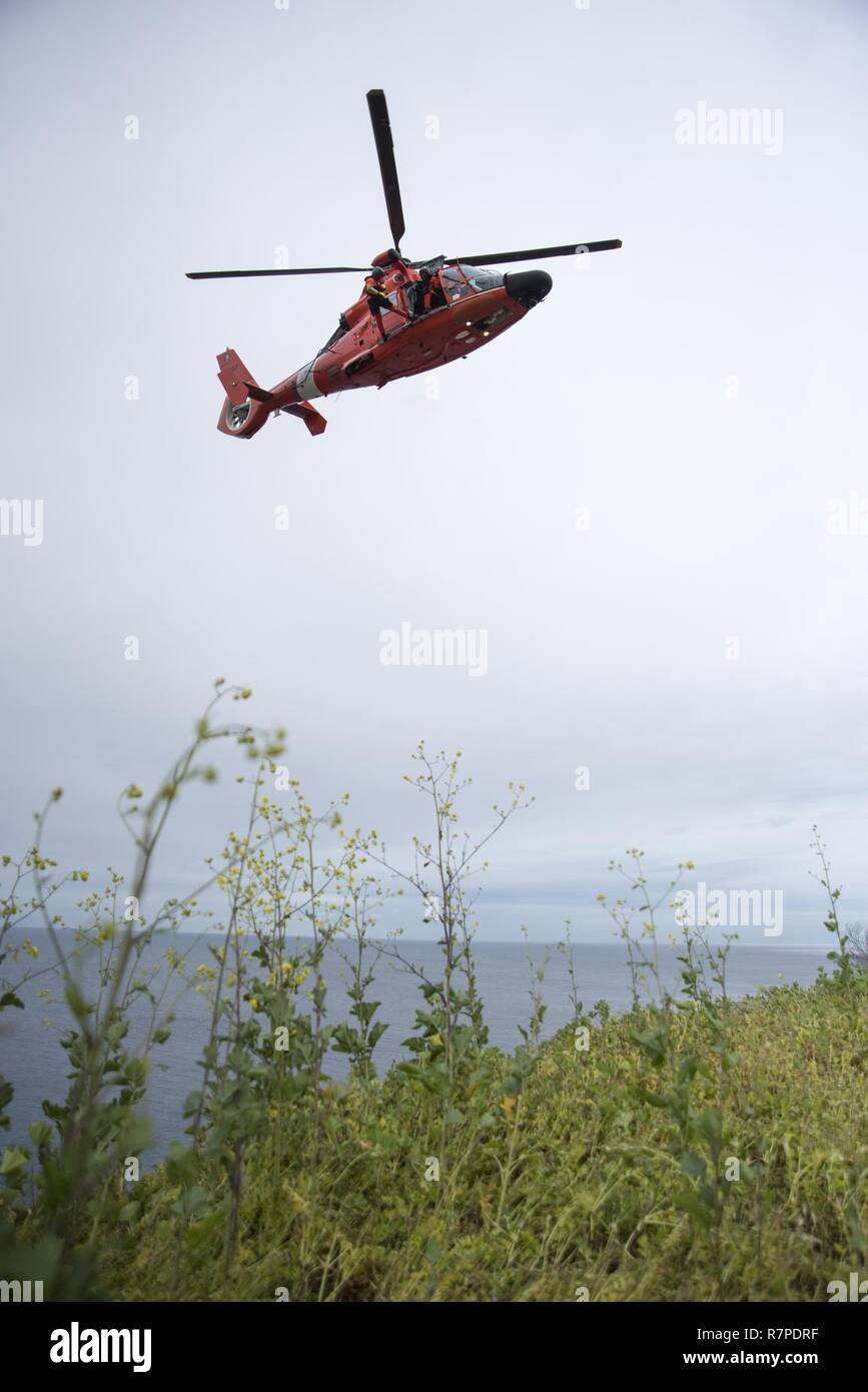 Un nageur de sauvetage de la Garde côtière canadienne affectée à la base d'opération avancée Point Mugu est abaissé d'un MH-65 hélicoptère Dauphin sur une falaise au cours de la formation en sauvetage au point Vicente Lighthouse 21 mars 2017. La formation permet de garder d'équipage compétent dans le cas d'un monde réel côté falaise de sauvetage. Banque D'Images