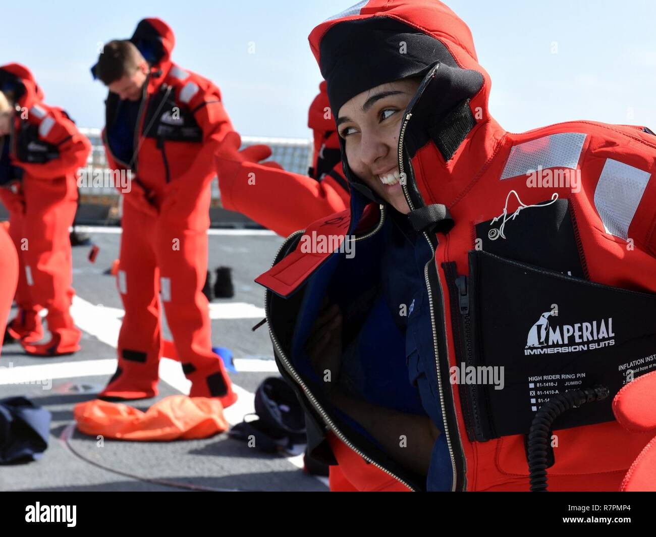 Seaman Apprentice Elizabeth Terrazas, l'équipage d'un les garde-côte de Munro, gloussements lors de courses à ses camarades de don une combinaison d'immersion en eau froide pendant qu'ils sont en cours, Mars 26, 2017. L'équipage n'avait que 60 secondes pour mettre rapidement et précisément sur leurs costumes, simulant la préparation à l'abandon du navire en cas d'urgence. La Garde côtière américaine Banque D'Images