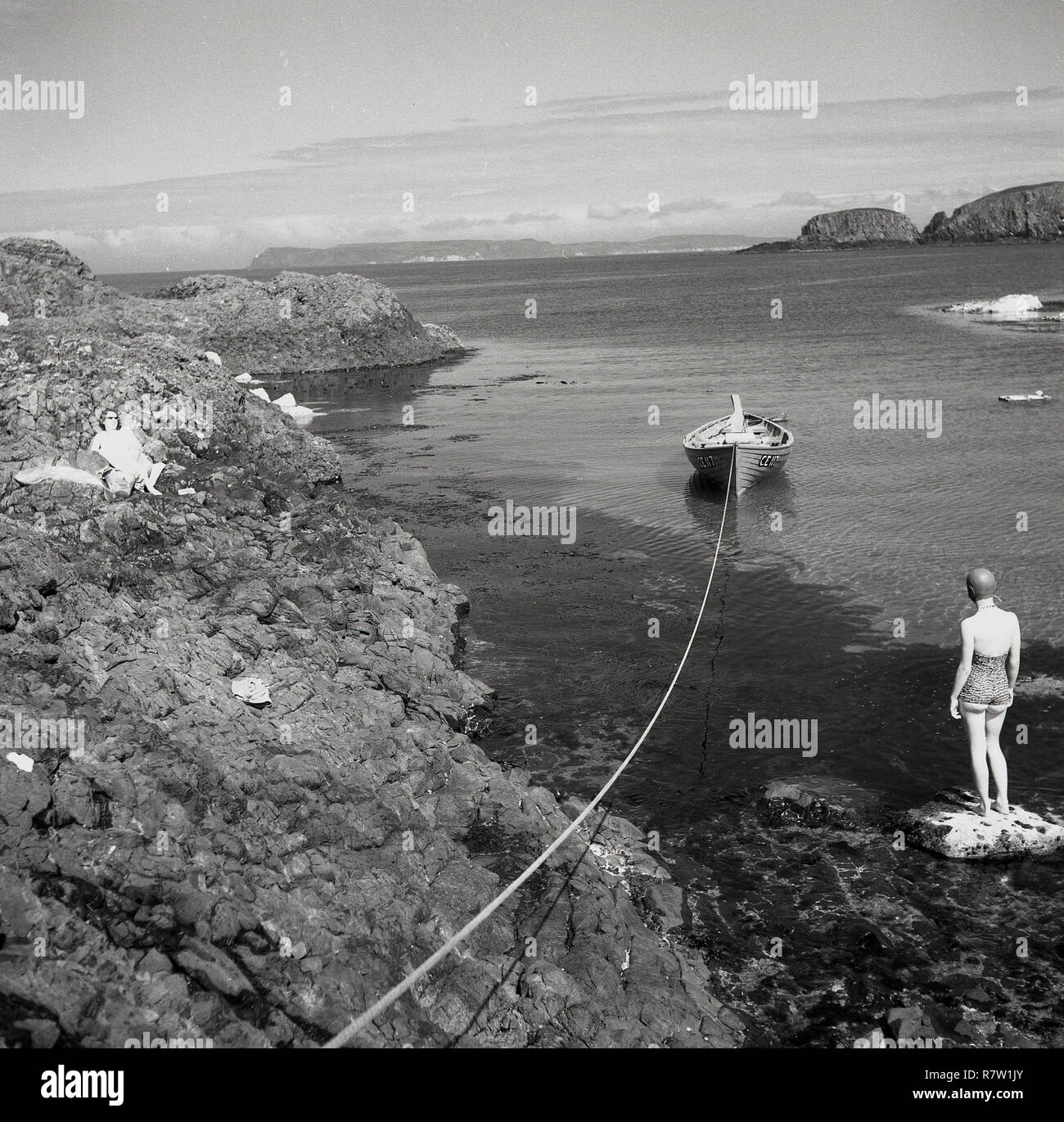 Années 1950, historique, à la Côte d'Antrim, Irlande du Nord, deux femmes baigneurs sur les rochers dans une petite baie ou couvrir, l'un debout dans un court de l'époque et maillot de bain en caoutchouc hat au bord de l'eau. Banque D'Images