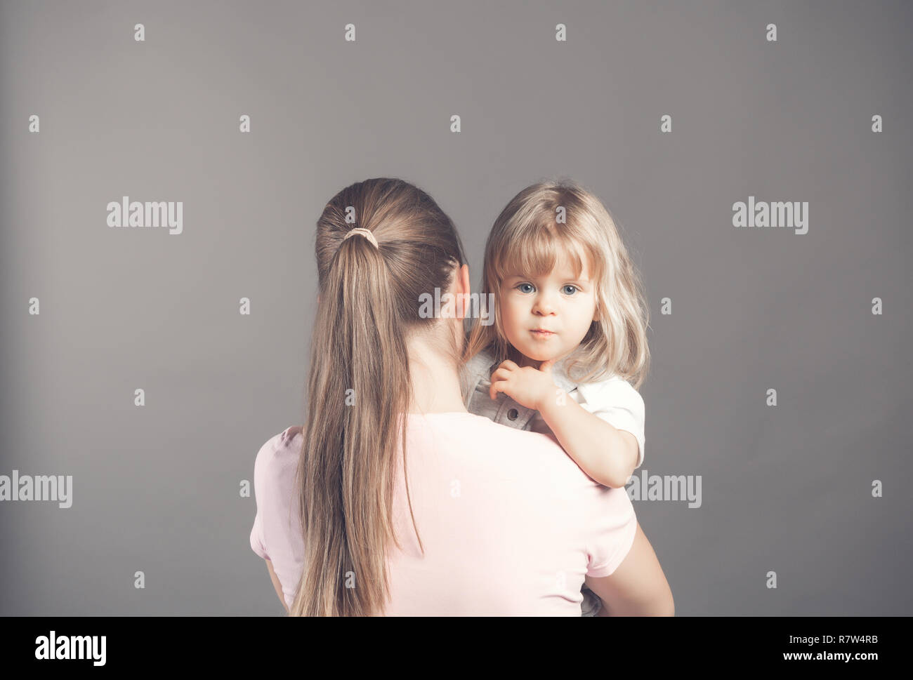 Et les jeunes peuplements mère slim avec son dos et tient dans ses bras un petit enfant merveilleux. Adorable blonde blue eyed baby girl est à la recherche à l'appareil photo Banque D'Images