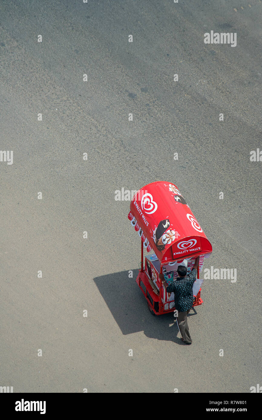 Ci-dessous sur une route goudronnée un homme seul commerçant rue rouge vif pousse son chariot le long de la crème glacée. Banque D'Images