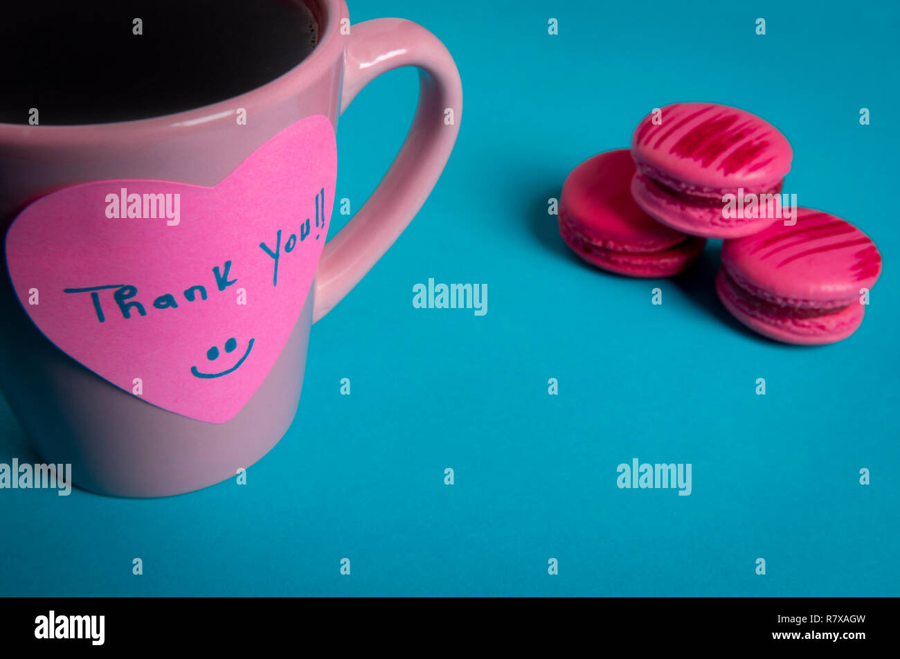 Tasse à café et macarons roses sur fond bleu. Note papier avec un message de remerciement fixés sur la tasse de café Banque D'Images