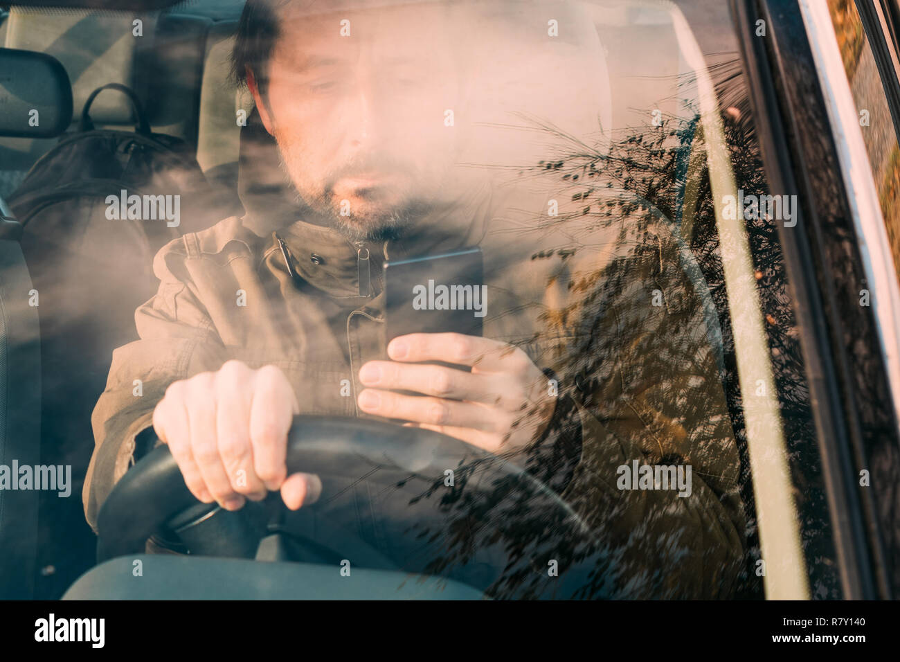 Vue avant de l'homme conduisant voiture et SMS sur téléphone mobile qui est un comportement téméraire et dangereux Banque D'Images