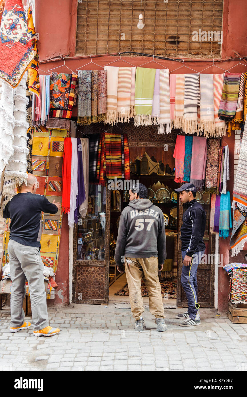 05-03-15, Marrakech, Maroc. Scène de rue dans le souk, dans la médina. Les jeunes hommes se tiennent à l'extérieur d'un magasin qui vend des tissus de couleurs vives. Photo : © Carte SIM Banque D'Images