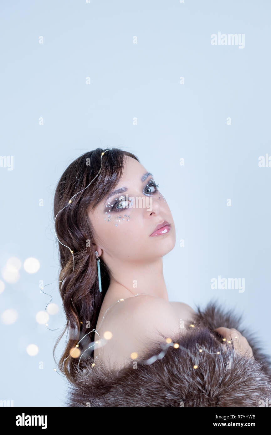 Close-up portrait of Beautiful woman with curly art parfait maquillage, visage givré à la mode,design yeux avec des paillettes perles,pierres, font de la décoration. Guirlande de Noël lumières.Eco manteau de fourrure.yeux expressifs.Copy space Banque D'Images