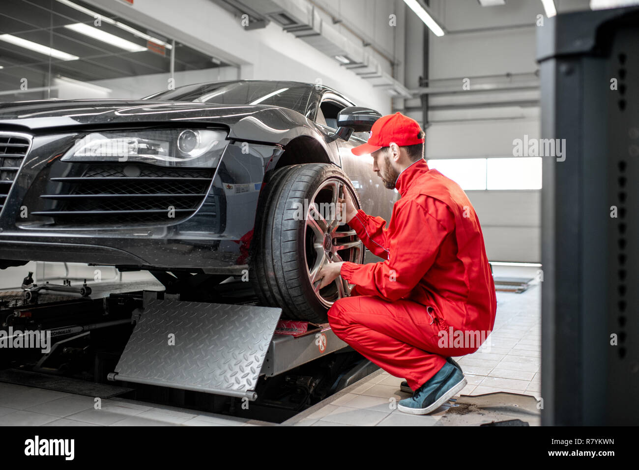 Service de voiture travailleur dans l'uniforme rouge changer volant d'une voiture de sport au service de montage des pneus Banque D'Images
