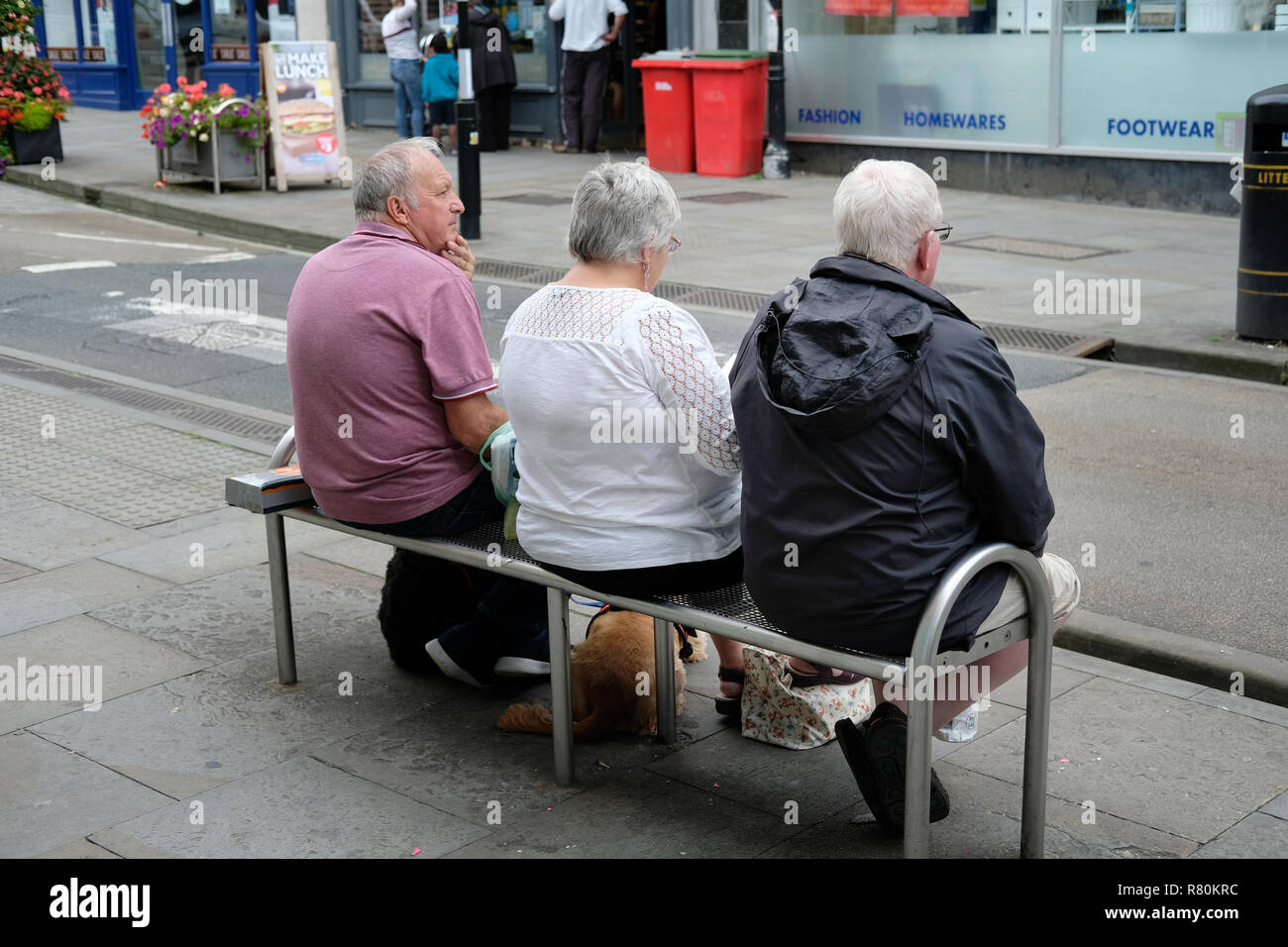 Trois retraités assis sur un banc sur un hight street, à Wells, Somerset. Banque D'Images