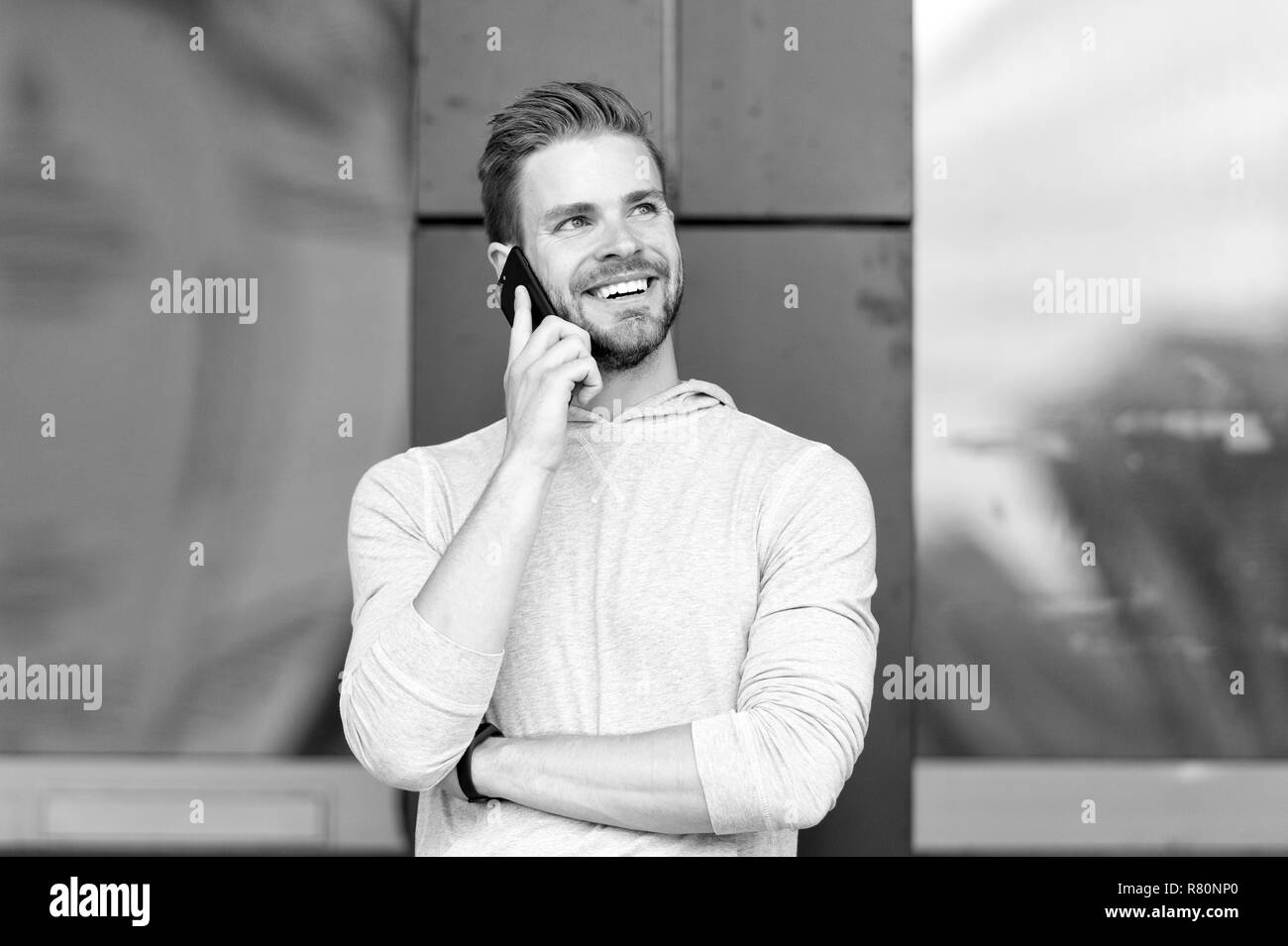 Heureux de vous entendre. Barbu homme marche avec smartphone, contexte urbain. L'homme au visage souriant agréable parle sur smartphone. Guy heureux réponse appel sur smartphone. Conversation agréable avec un ami. Banque D'Images