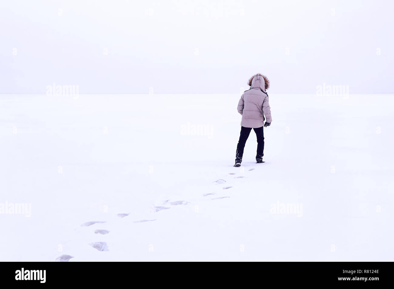 Homme marchant sur la neige, des traces de pas dans la neige, derrière. Le froid de l'hiver sibérien. La Russie. Le gars dans la veste d'hiver avec une capuche Down Jacket blanc. Banque D'Images