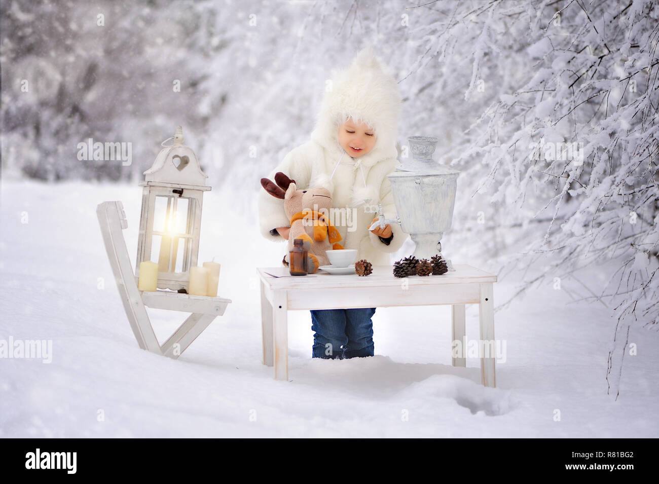 L'enfant dans un manteau en peau de mouton blanc et bouchon, ouvre un cadeau et décore l'arbre de Noël dans une forêt couverte de neige de l'hiver. Un arbre de Noël est Banque D'Images