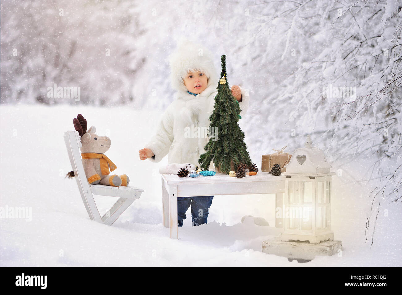 L'enfant dans un manteau en peau de mouton blanc et bouchon, ouvre un cadeau et décore l'arbre de Noël dans une forêt couverte de neige de l'hiver. Un arbre de Noël est Banque D'Images