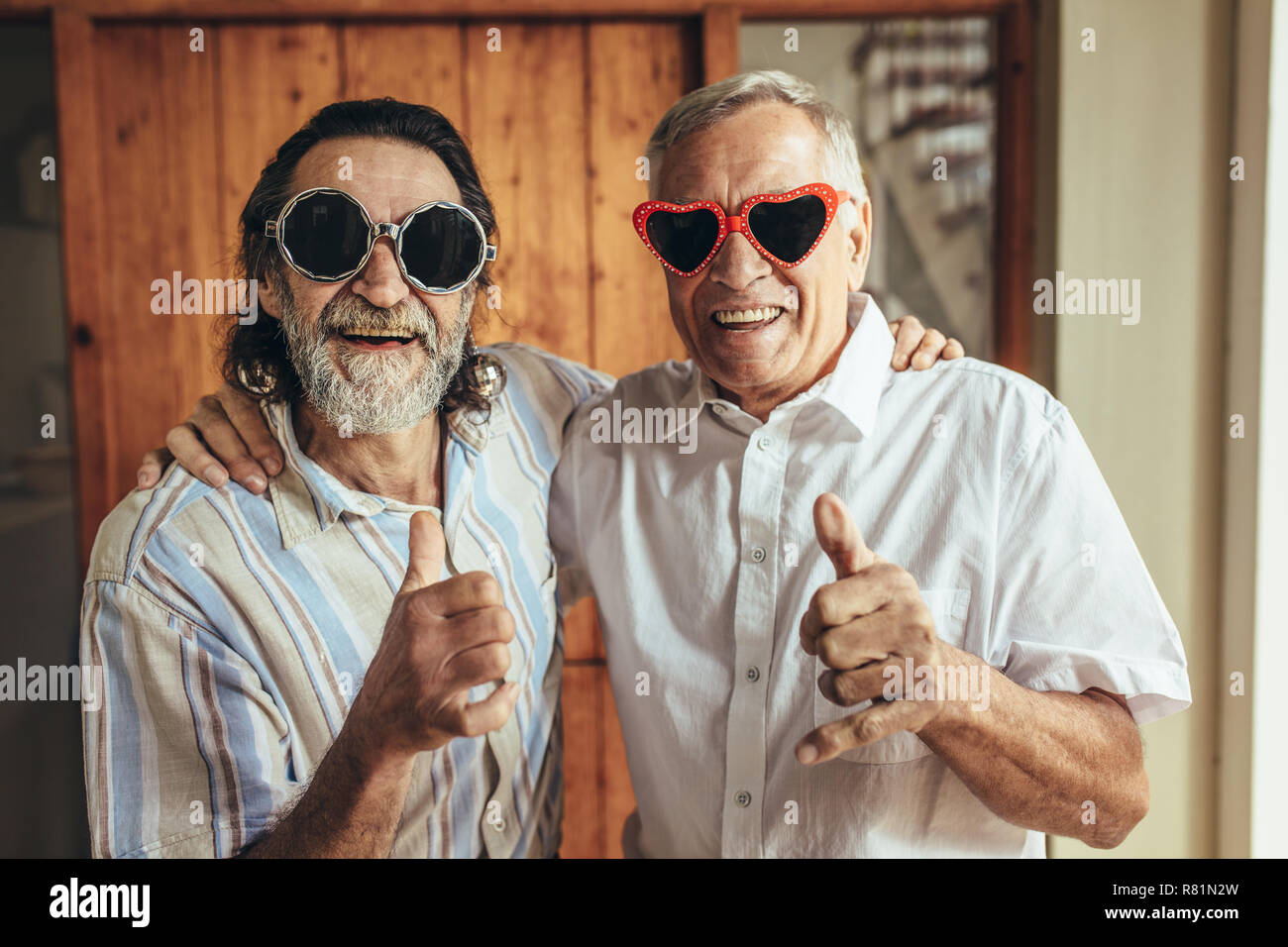 Heureux les hommes âgés portant des lunettes drôles showing Thumbs up. Amis retraités avec partie eyewear giving Thumbs up. Banque D'Images