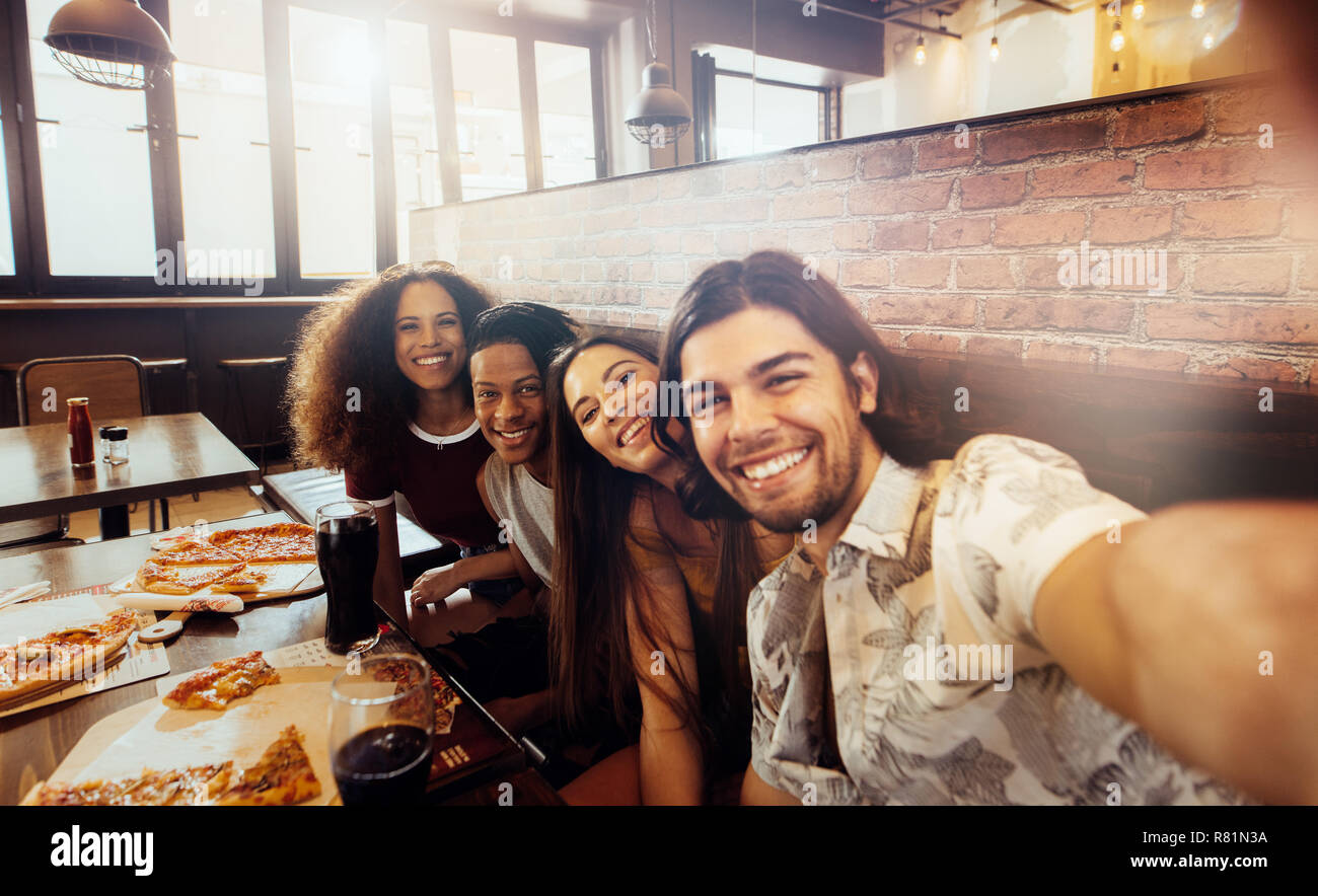 Jeune homme en tenant avec selfies amis assis au café. Groupe d'amis multi-ethnique au restaurant de la capture d'un moment dans l'appareil photo. Banque D'Images