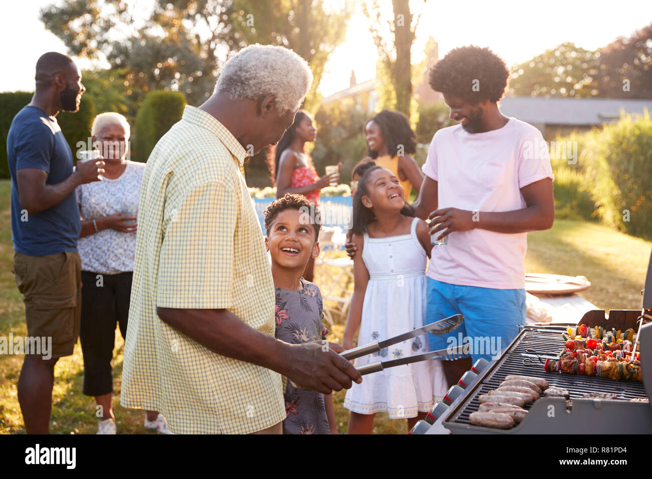 Grand-père et petit-fils de parler par le grill à un barbecue familial Banque D'Images