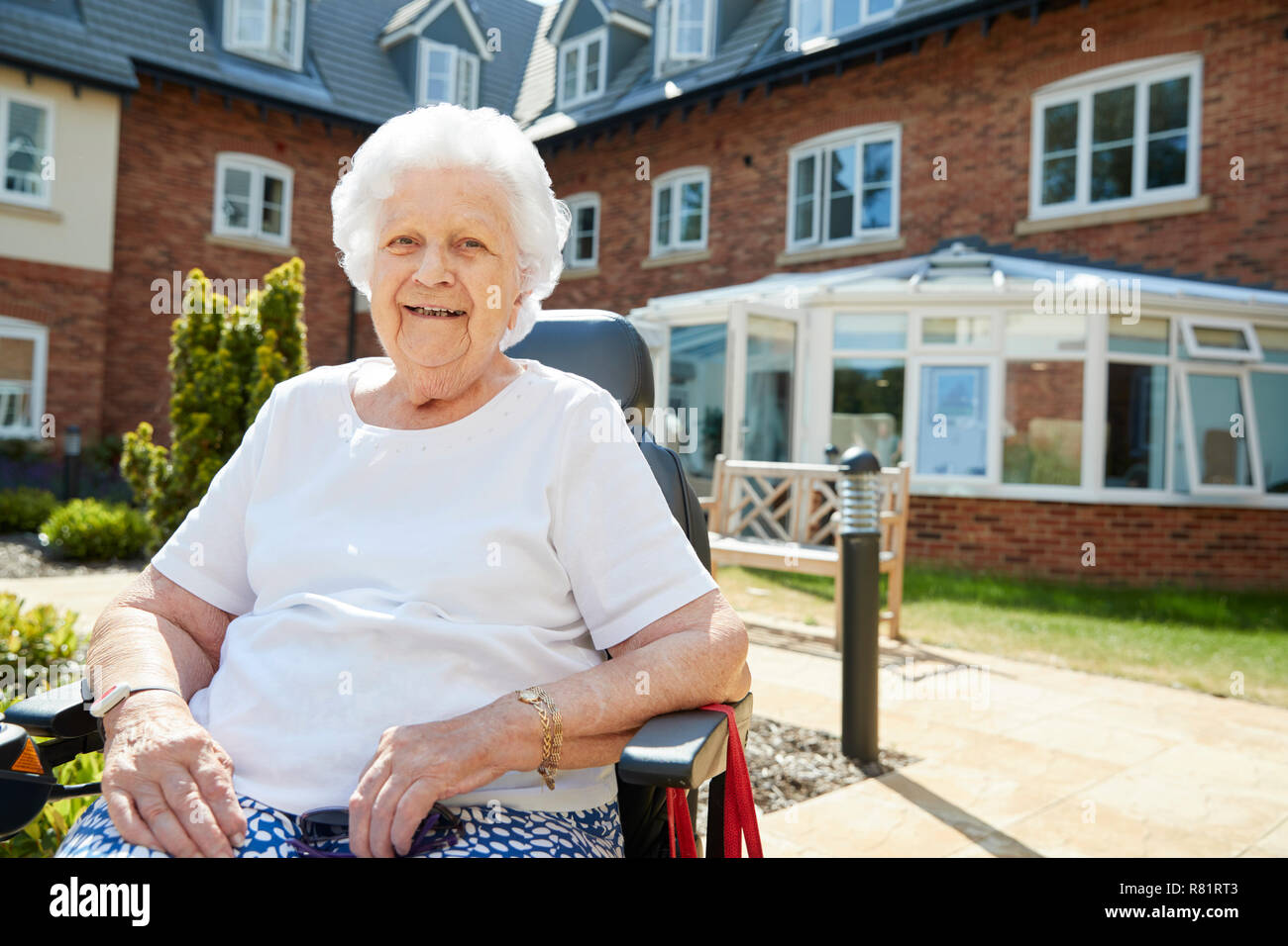 Portrait of Senior Woman Sitting hors Maison de Retraite en fauteuil roulant motorisé. Banque D'Images