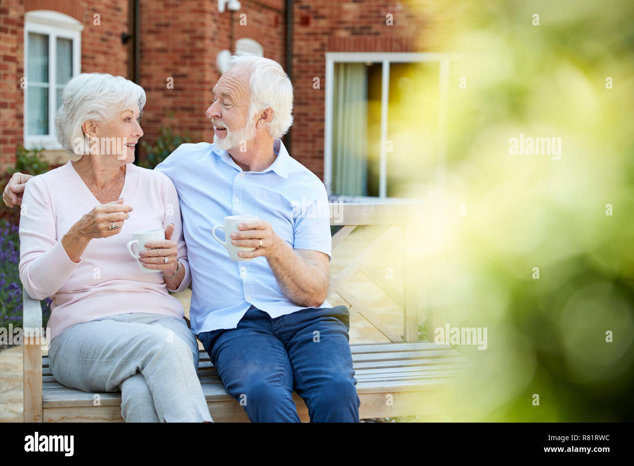 Couple de retraités assis sur un banc avec boisson chaude en résidence-services Banque D'Images
