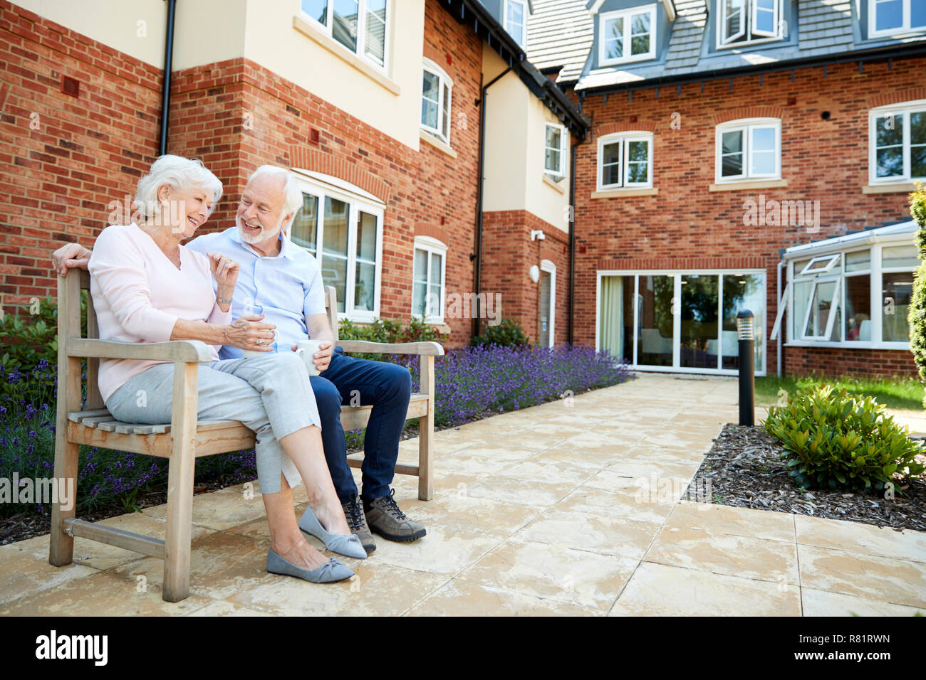 Couple de retraités assis sur un banc avec boisson chaude en résidence-services Banque D'Images