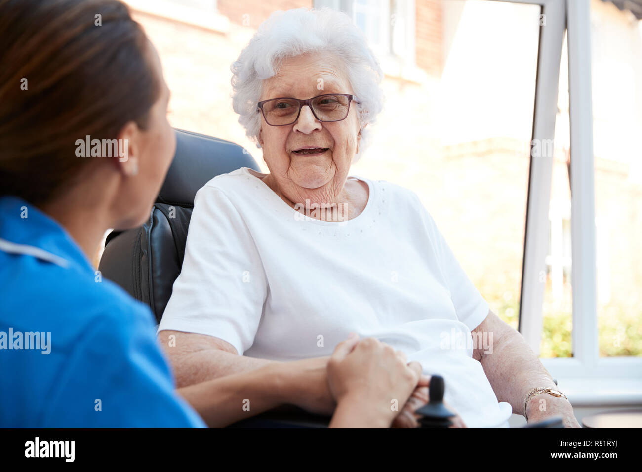 Hauts Femme assise en fauteuil roulant motorisé de parler avec l'infirmière en maison de retraite Banque D'Images