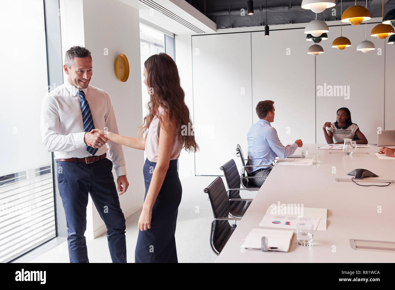 Businessman And Businesswoman Shaking Hands en salle de réunion moderne avec des collègues autour de la table en arrière-plan Banque D'Images